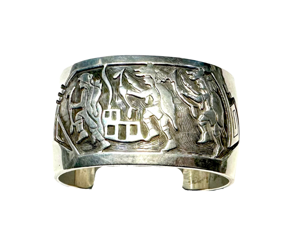 A silver bracelet with a carved scene depicting figures engaged in a dance or celebration.