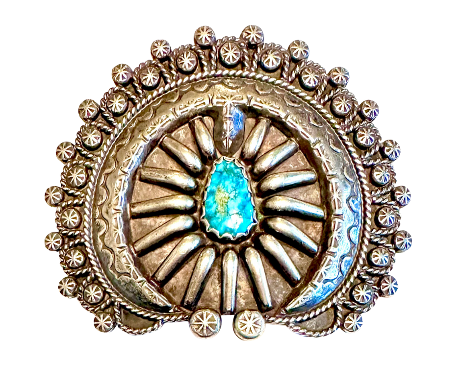 Round decorative metal brooch with intricate details and a central turquoise stone.