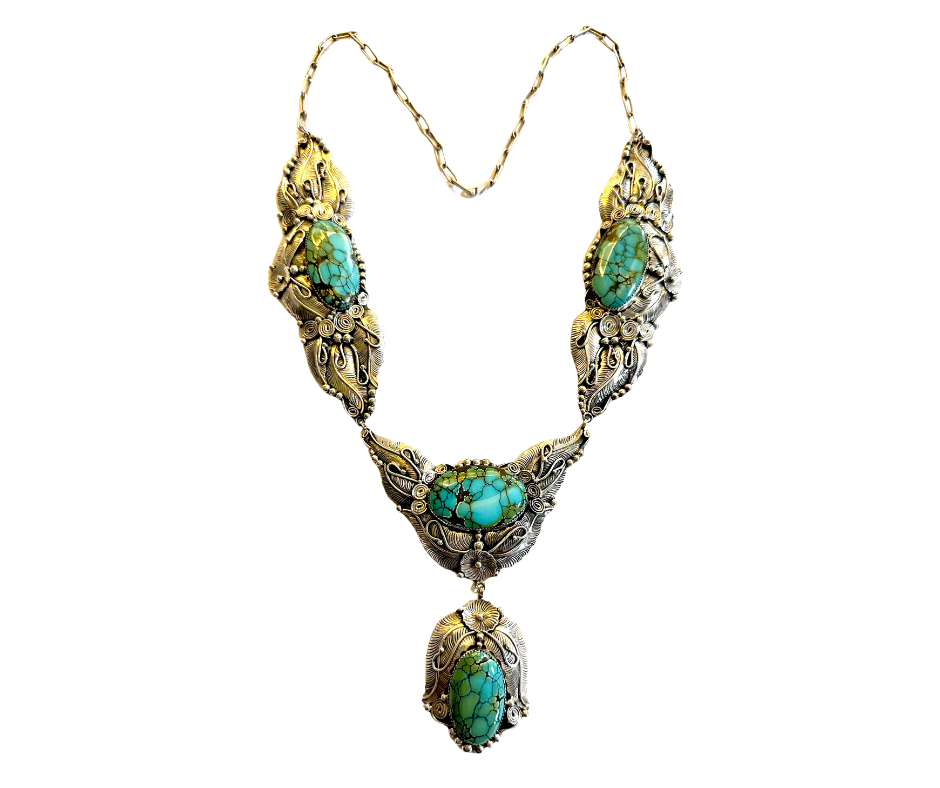 A silver necklace with turquoise stones and intricate ornamental details, featuring a large drop-shaped turquoise pendant.