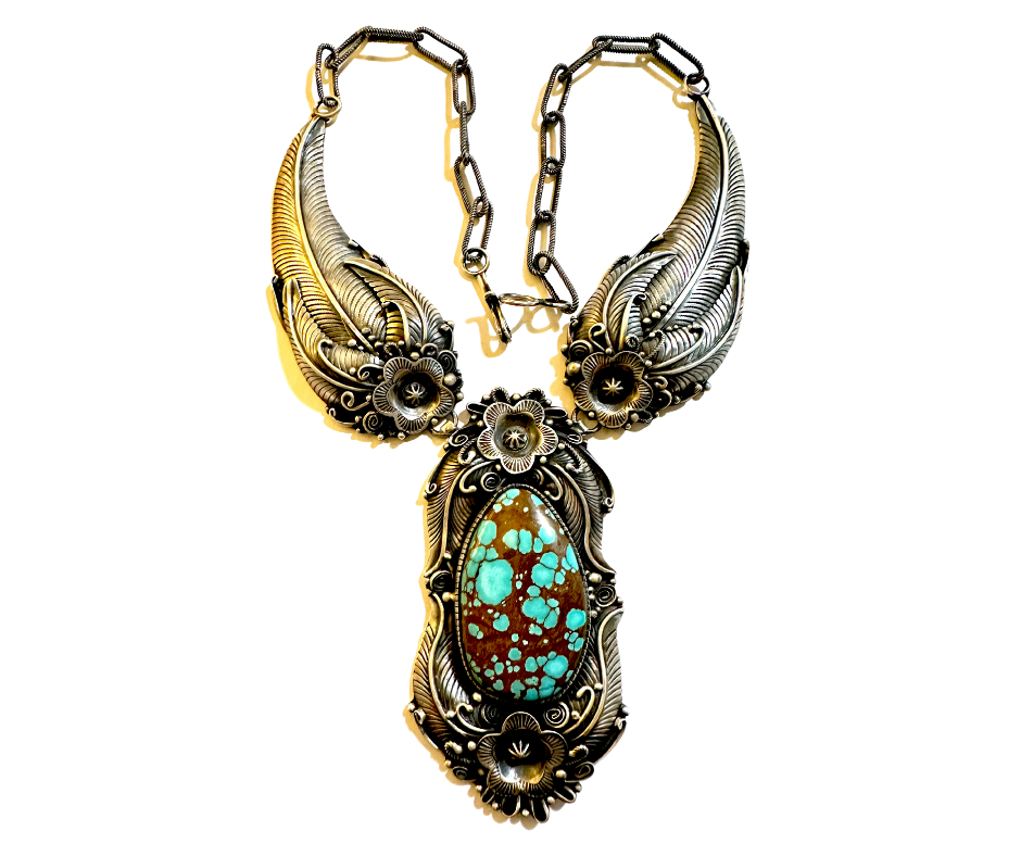 An ornate silver and gold necklace featuring a large turquoise stone surrounded by intricate floral and feather designs.
