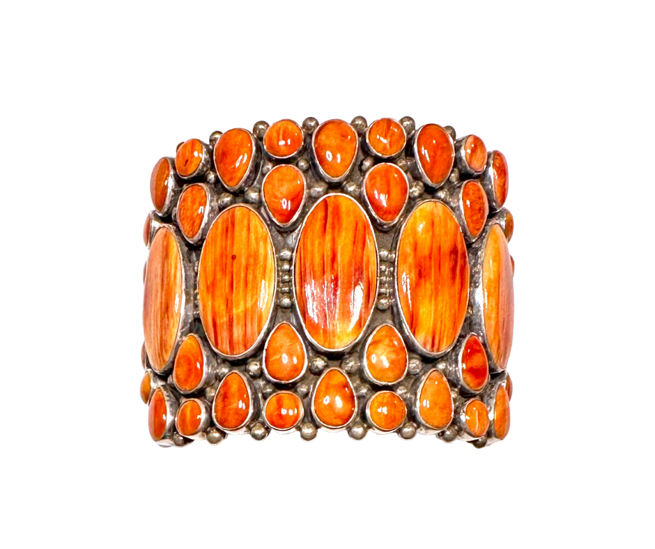 A decorative cuff bracelet with large oval and small round orange stones set in a metal band.