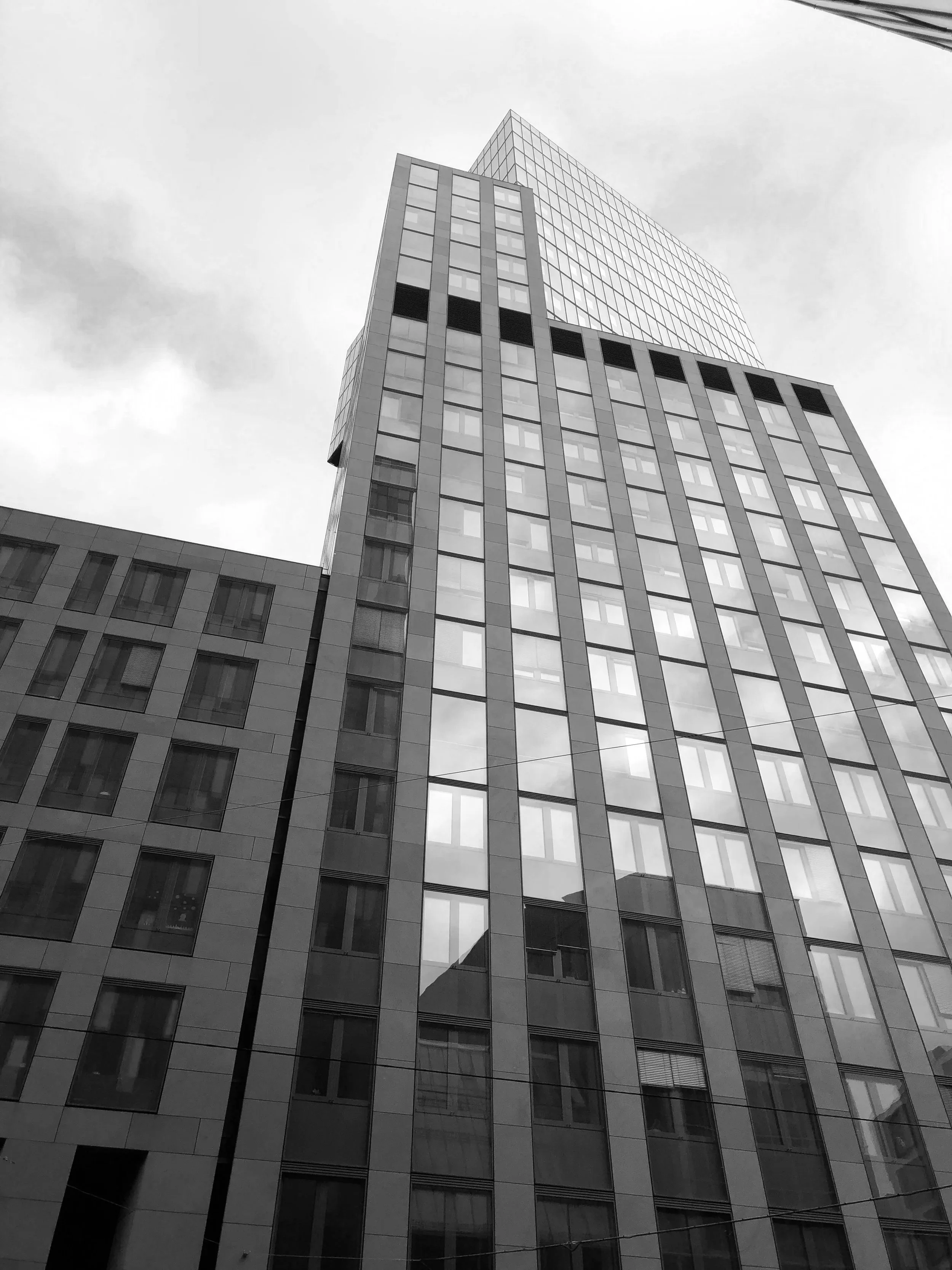 Tall modern office building with reflective glass windows in black and white, viewed from ground level looking up.