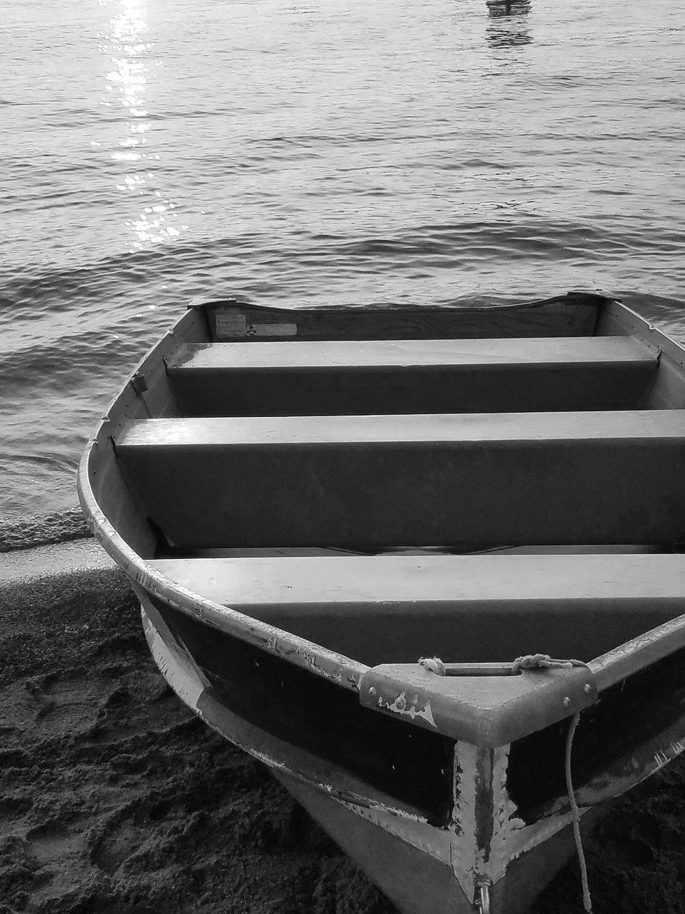 A small boat resting on the sandy shore next to calm water, with the sun's reflection visible on the water.