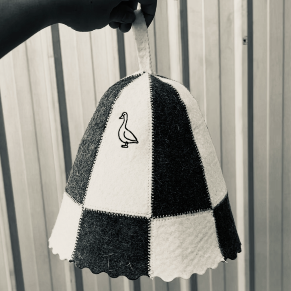 A black and white checkered fabric lampshade with an embroidered goose on one panel, hanging in front of a metal wall.