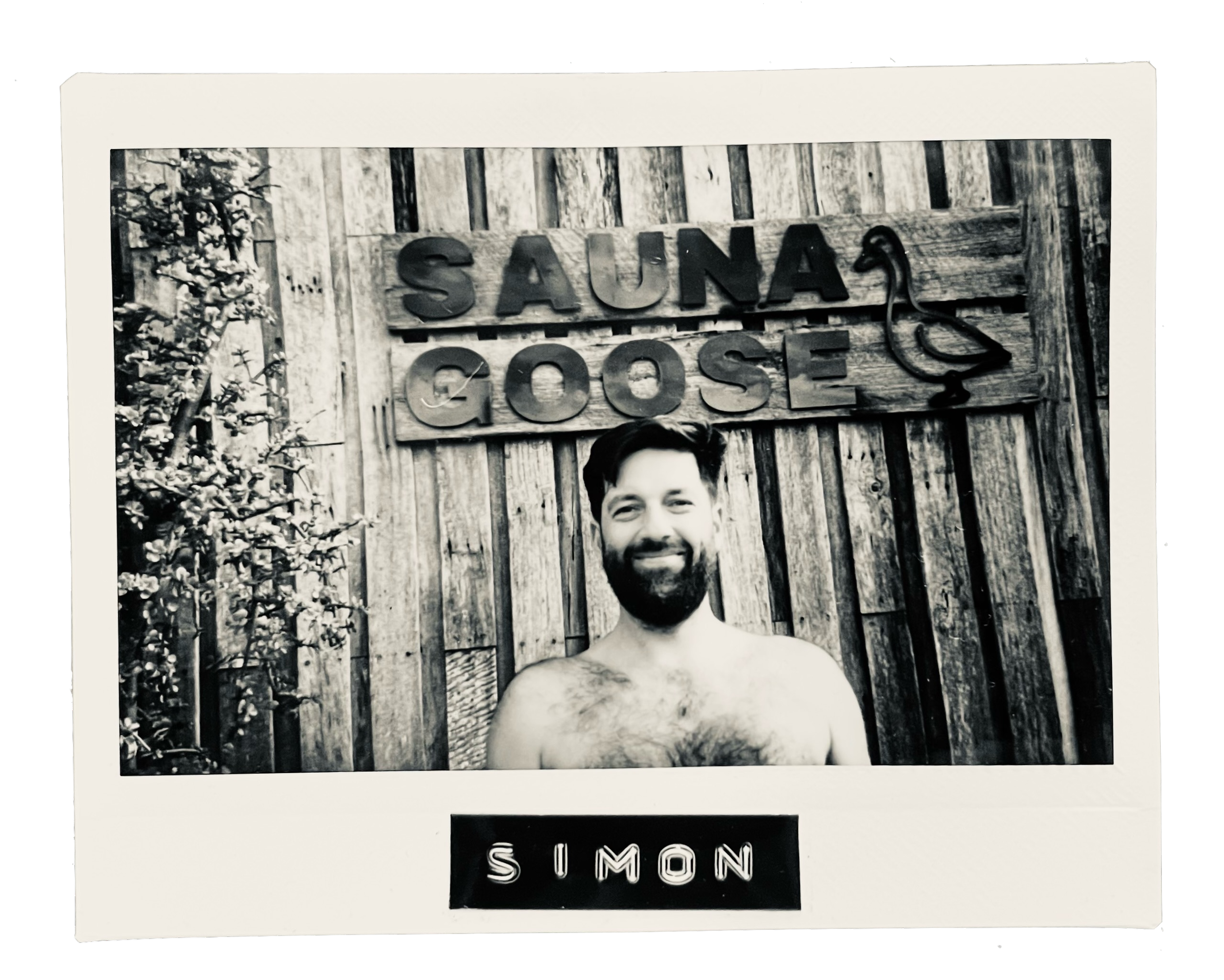 Black and white photo of a smiling man with a beard and shirtless, standing in front of a wooden fence with a sign that reads 'Sauna Goose' and a goose-shaped hook. The name 'Simon' is inscribed on a plaque below the photo.