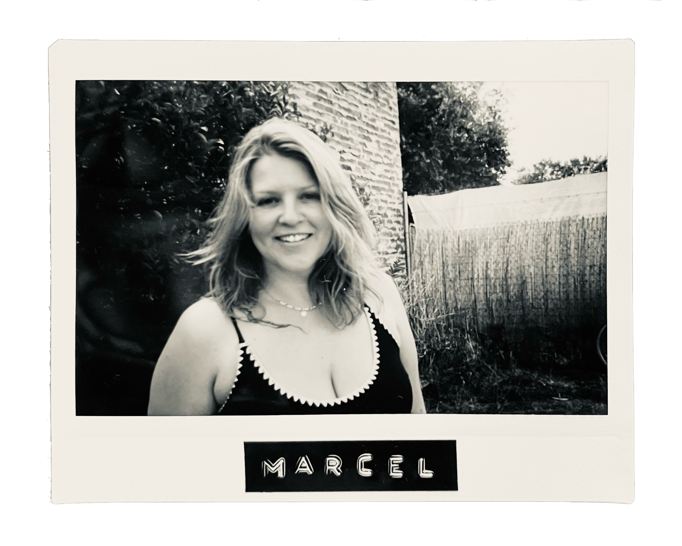 Black and white photo of a smiling woman with shoulder-length wavy hair, wearing a sleeveless top with decorative trim, outdoors with plants and a fence in the background, labeled "Marcel."