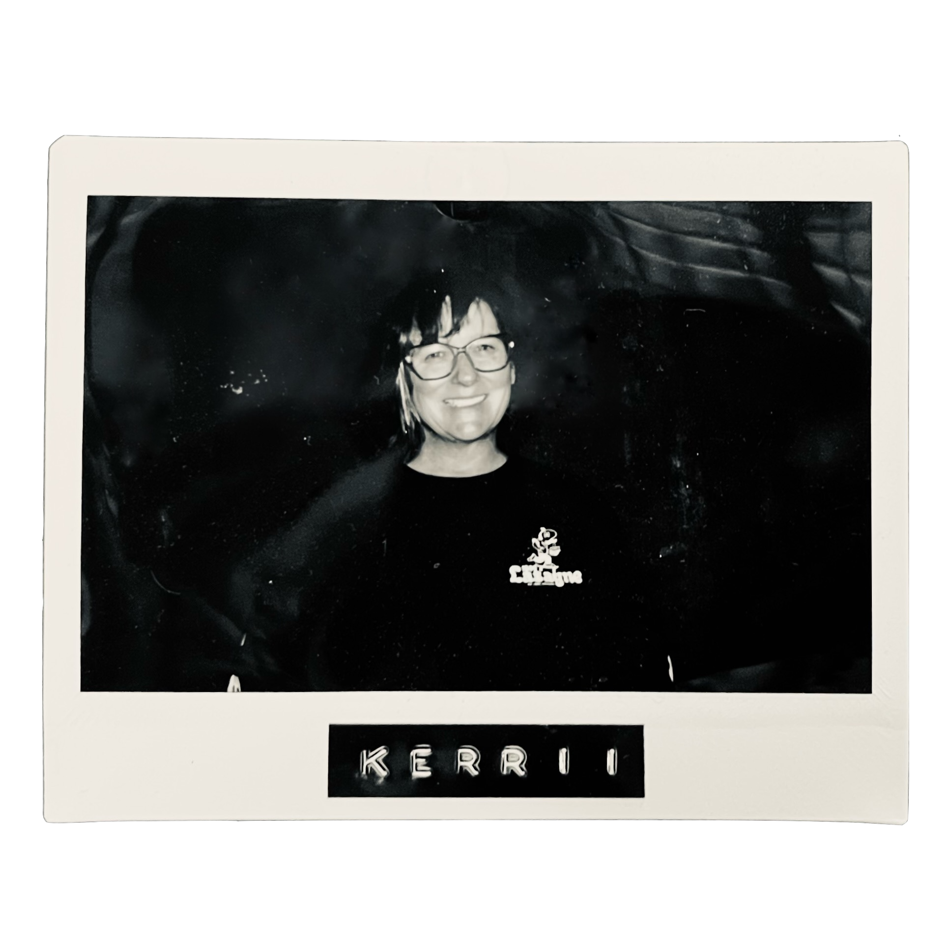 A black-and-white photo of a smiling woman with glasses and short hair, wearing a shirt with a logo. The photo has a white border with the name "KERRI" written at the bottom.