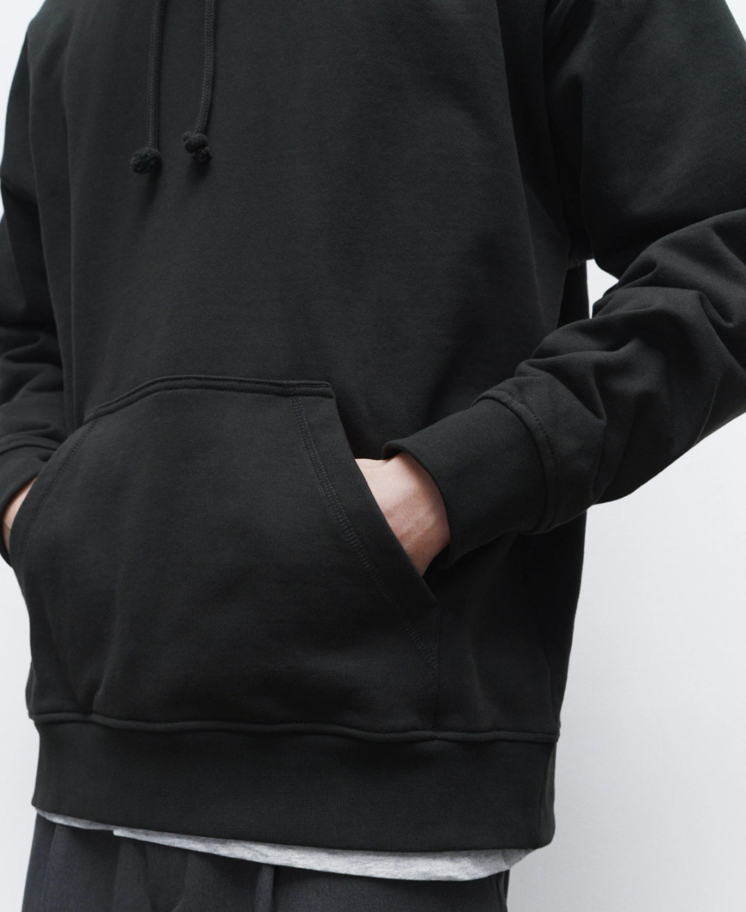 A person wearing a black hoodie with a front pocket and black drawstrings, standing against a plain white background.