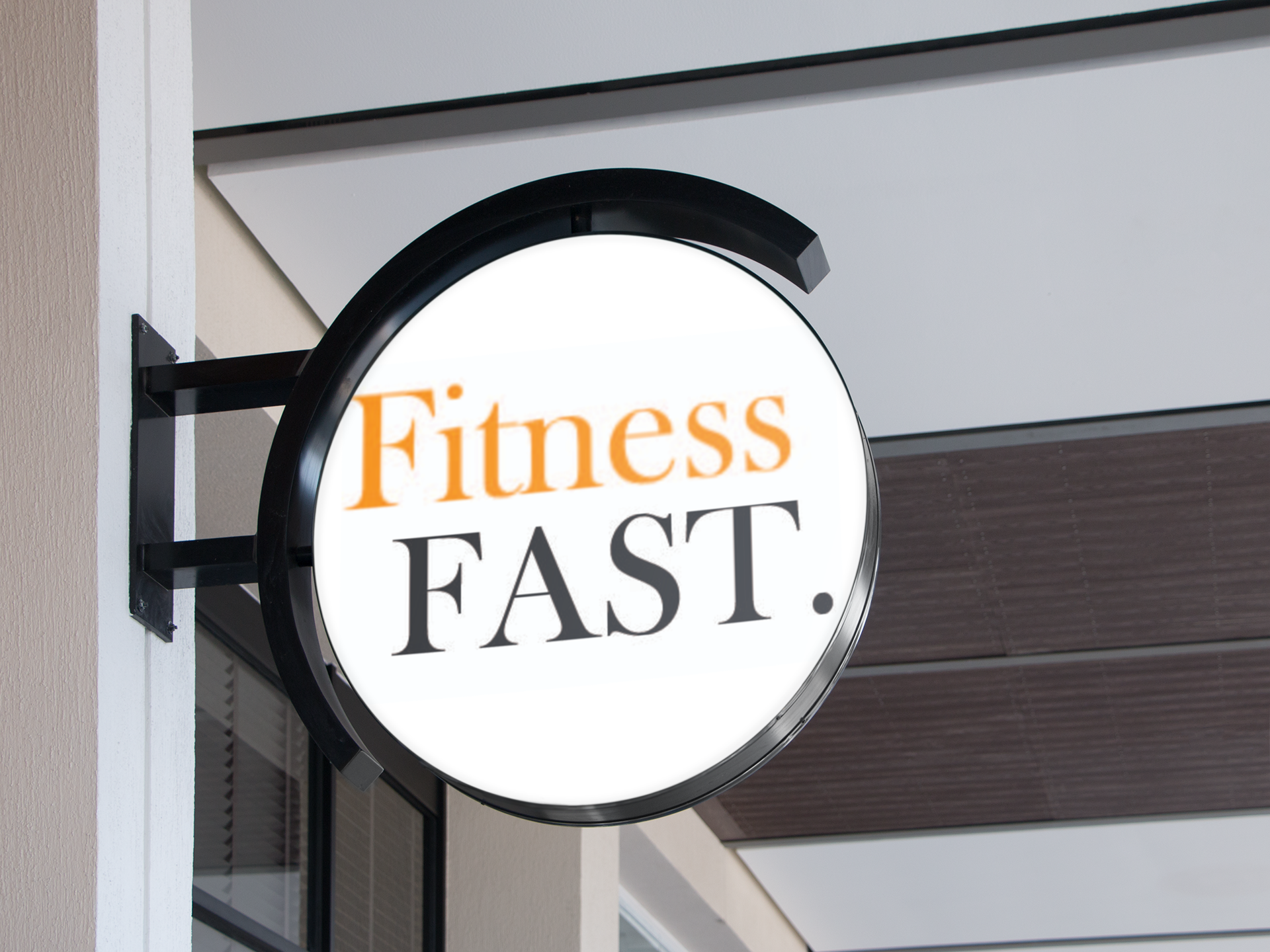 Round illuminated sign reading 'Fitness FAST.' in orange and black text, mounted outside a building.