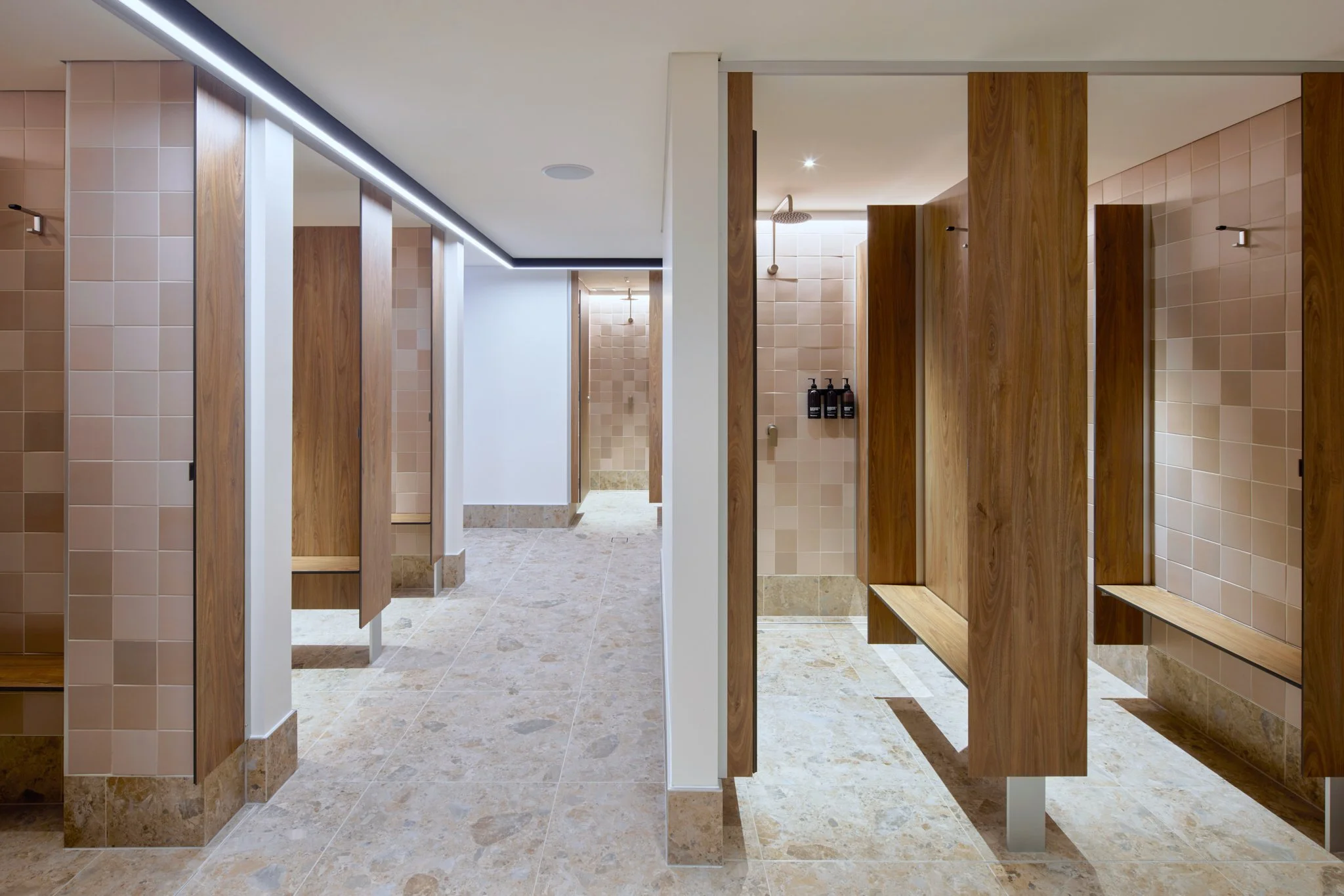 Modern men's locker room with wooden lockers, tiled walls, bench seating, and showerheads.