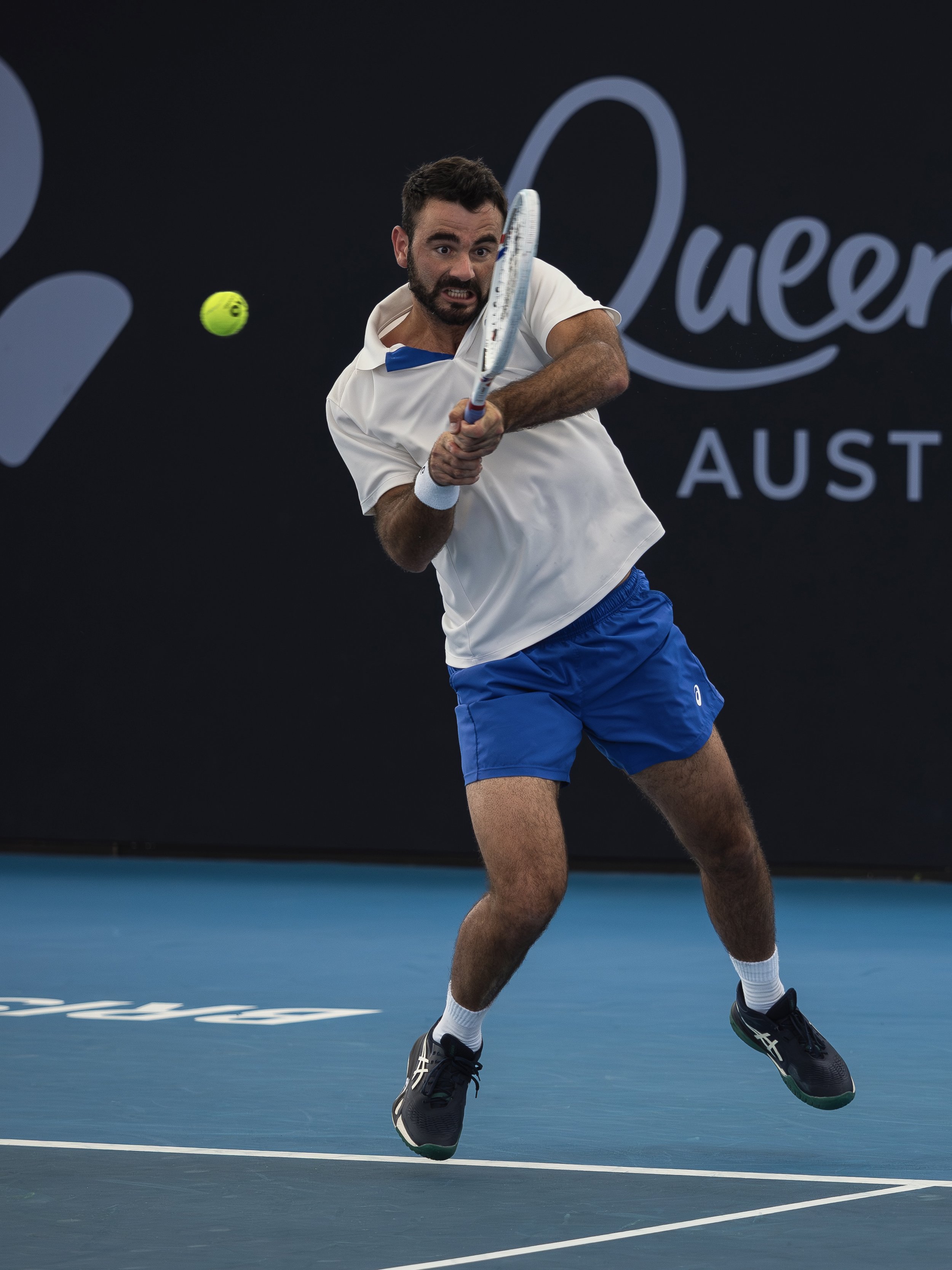 Male tennis player in motion hitting a tennis ball on an indoor court.