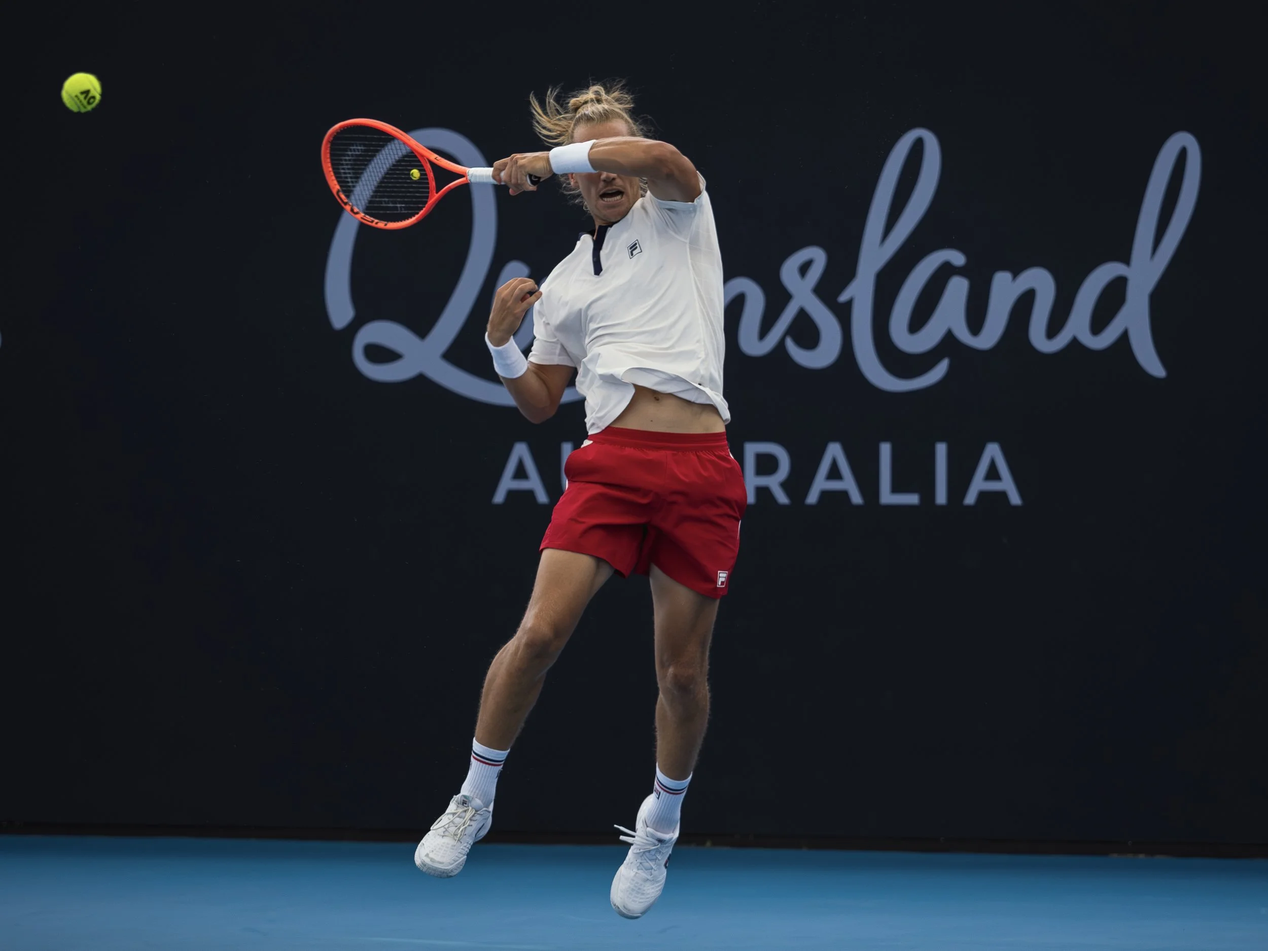 A female tennis player is mid-air preparing to hit a tennis ball with her racquet during a match at an Australian Open event.