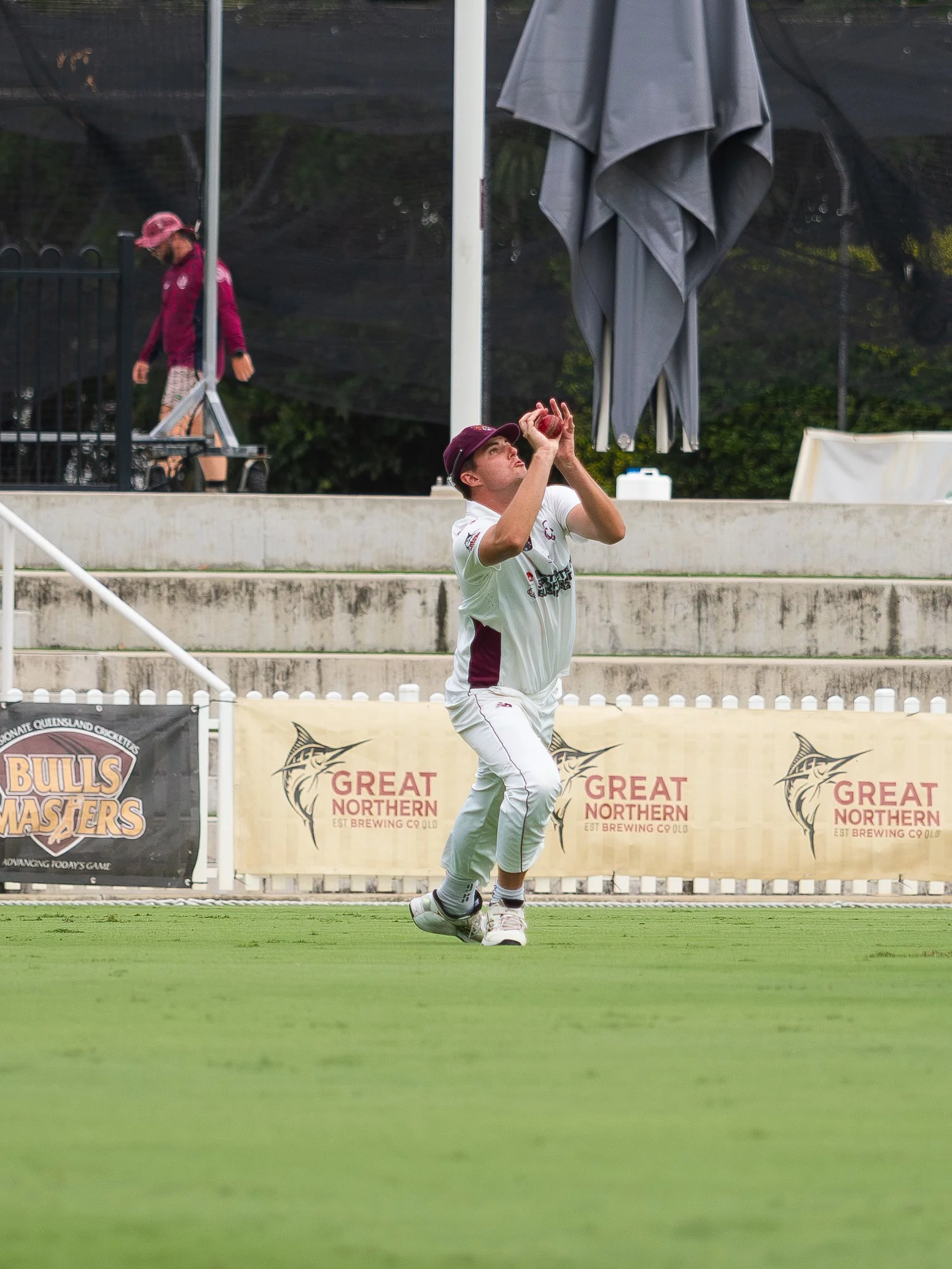 A man is playing cricket on a field, preparing to catch a ball that is falling from above.