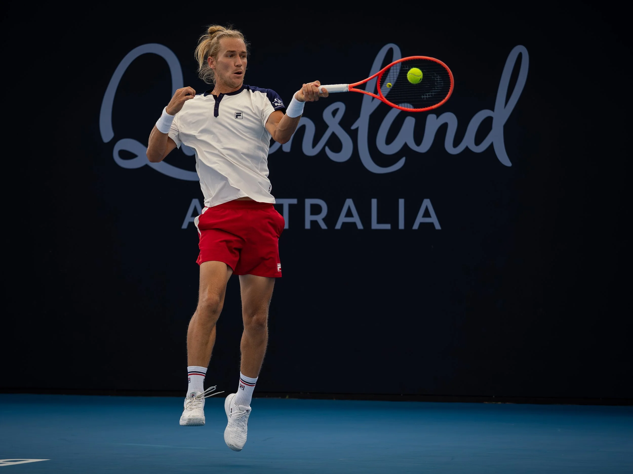 A tennis player in mid-air hitting a tennis ball with a racquet during a match at the Australian Open.