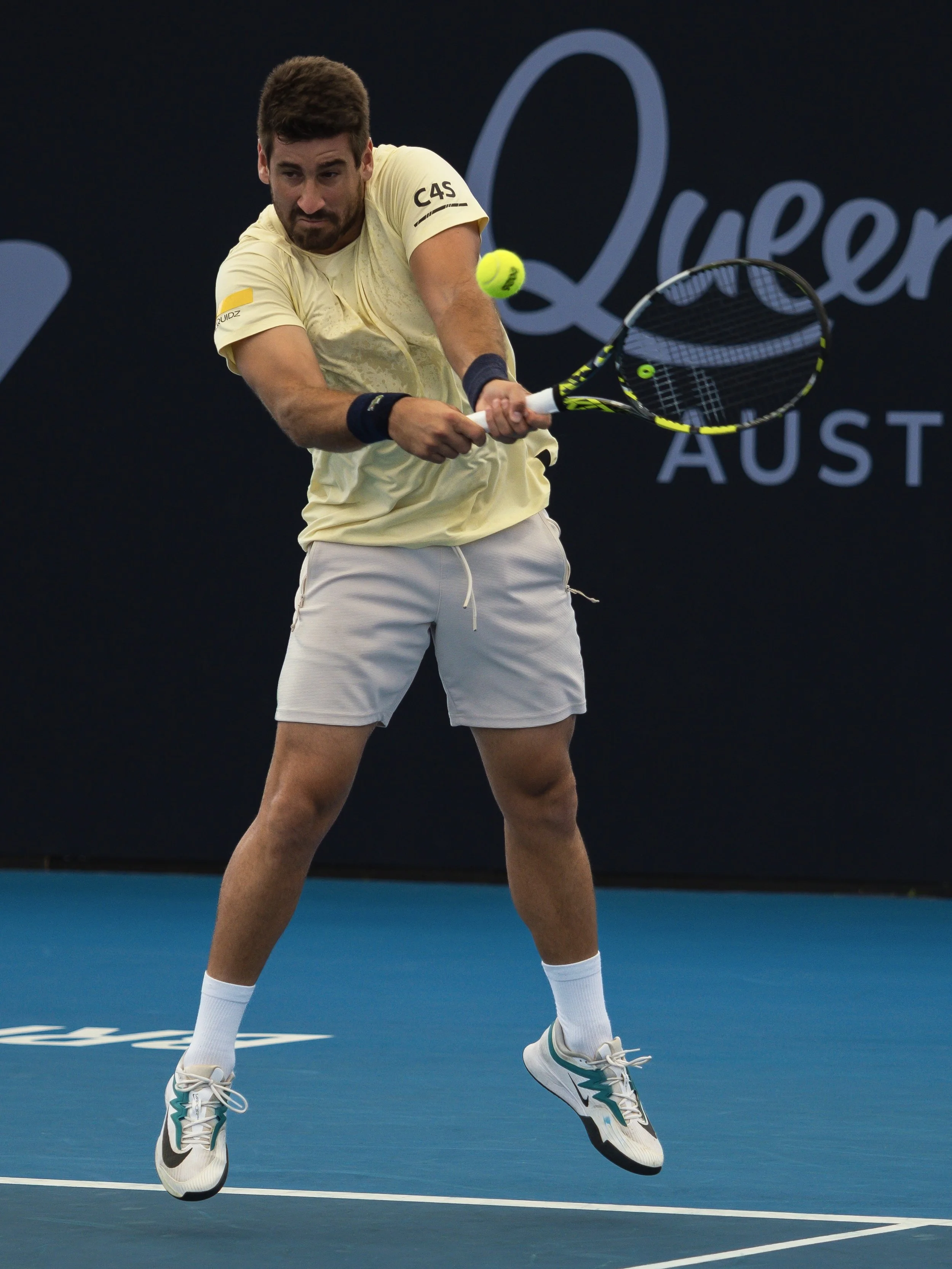A male tennis player in mid-air, hitting a tennis ball with his racket on a blue tennis court during a match at the Australian Open.