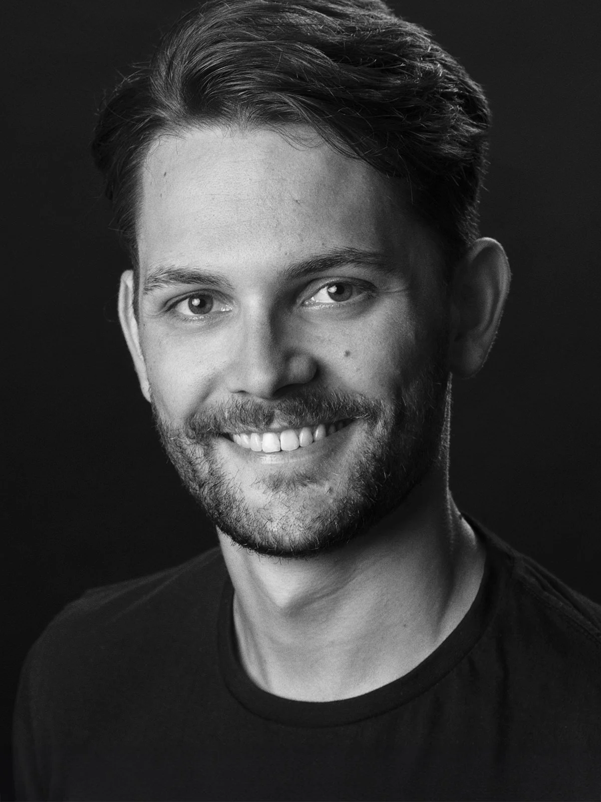 Foto einer jungen Mannes mit freundlichem Lächeln vor dunklem Hintergrund