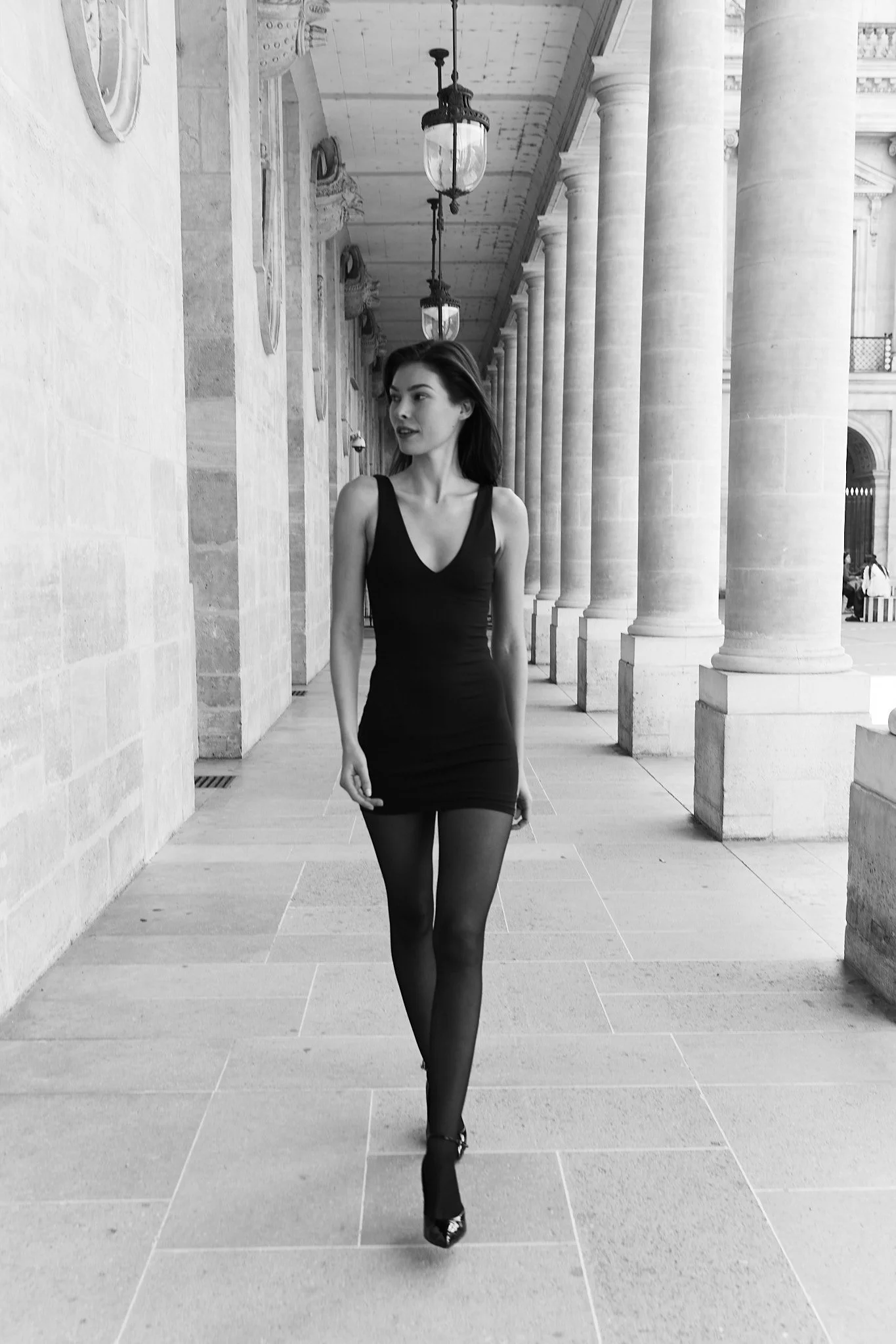 photo in black and white of a women model wearing black dress walking under the arch of palais royal for a fashion shoot