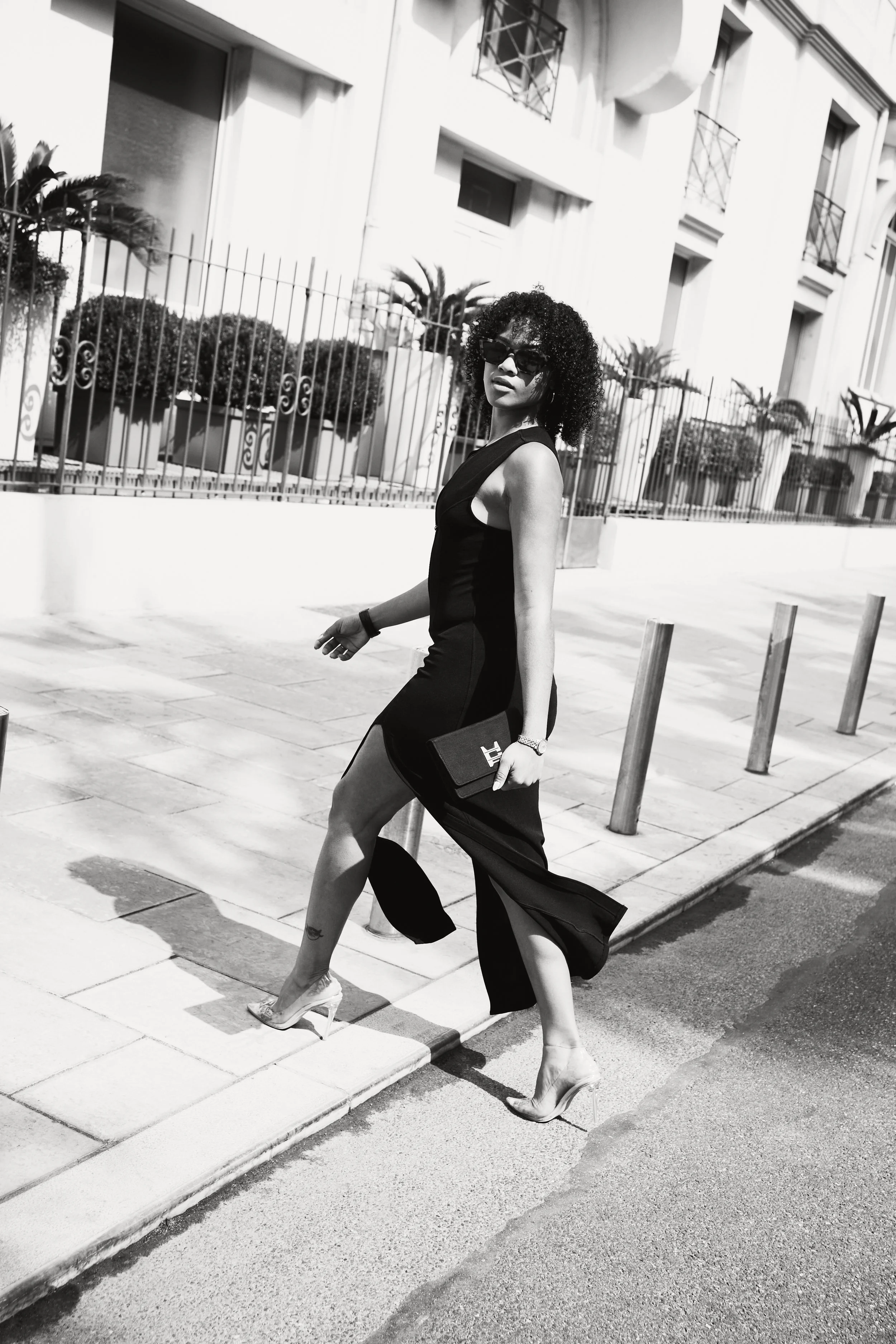 Photographie de mode noir et blanc à Cannes : mannequin en mouvement devant la façade du Majestic, portant une robe longue noire, des talons hauts et une pochette