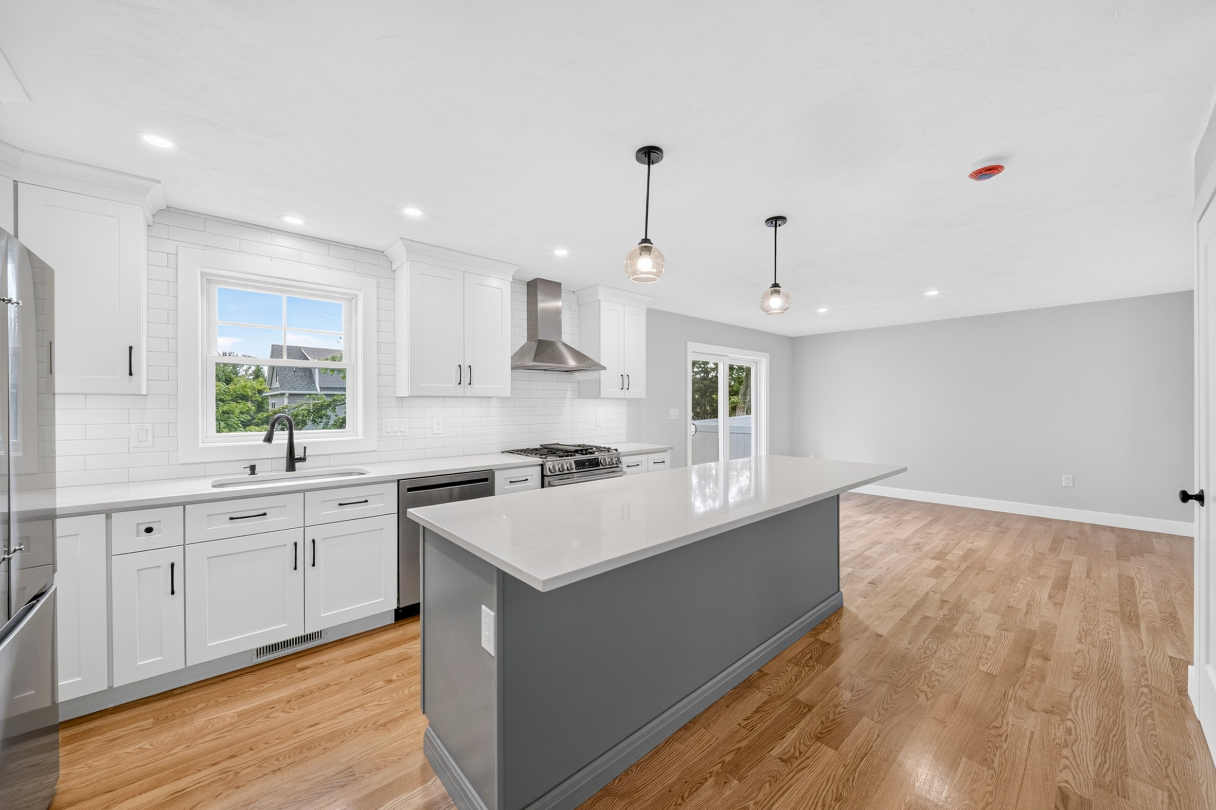 Modern kitchen in Billerica, MA, with white cabinets, a large white island, wood flooring, and pendant lights hanging from the ceiling.