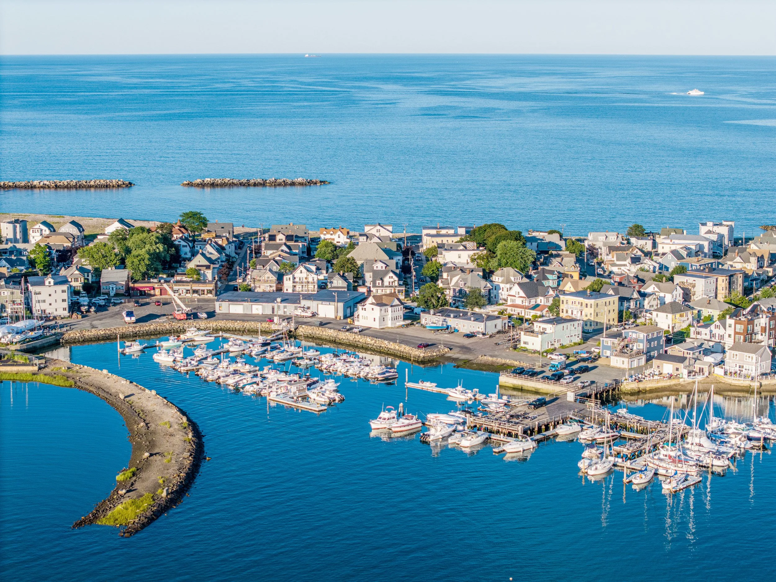 Aerial view of Winthrop, MA with boats in a marina, shoreline, houses, and the ocean extending to the horizon.
