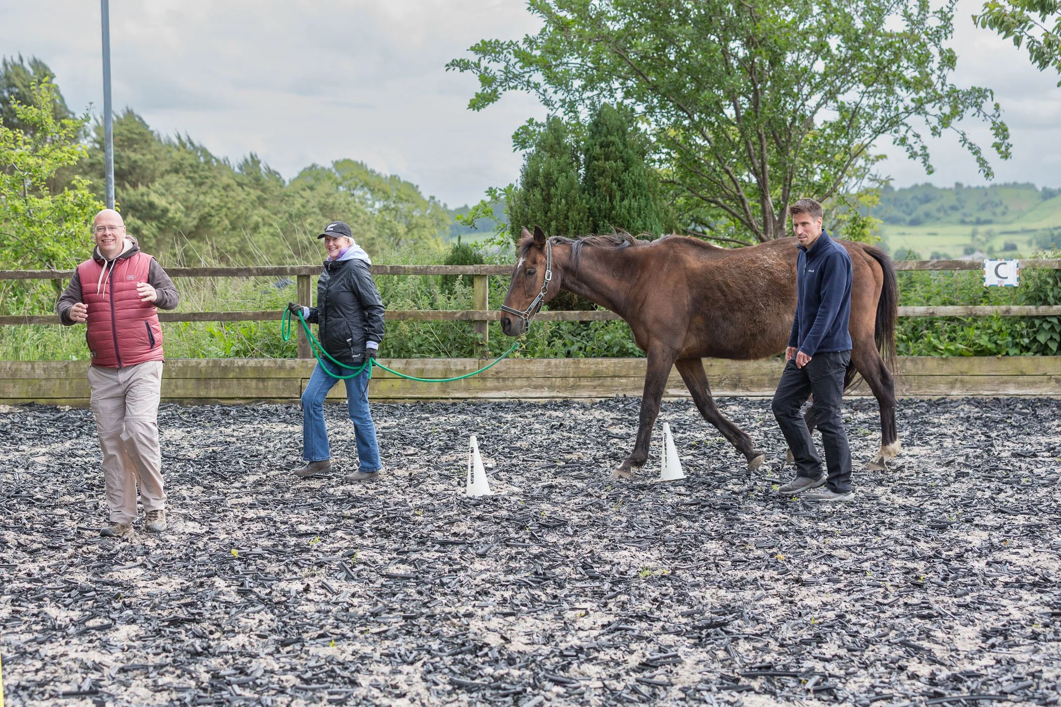 Three people lead a horse around an arena with trees in the background