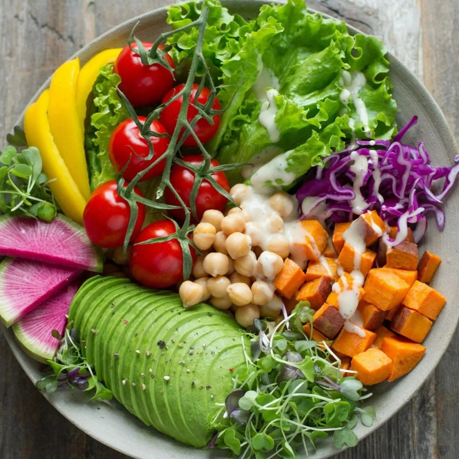 Bunter Gemüsesalat mit Tomaten, Avocado, Kürbis, rote Beete, Lollo Rosso, Kichererbsen, Wassermelone, Radieschen und Kresse auf einem Teller.