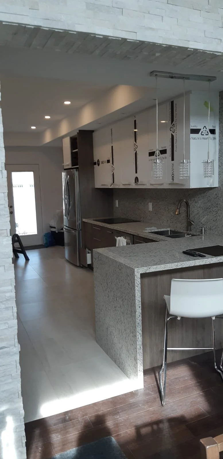 This kitchen renovation features crisp white cabinets paired with a quartz countertop with a waterfall edge, creating a clean and contemporary aesthetic. The kitchen floor is finished with 24 x 24-inch tiles, offering durability, easy maintenance, an