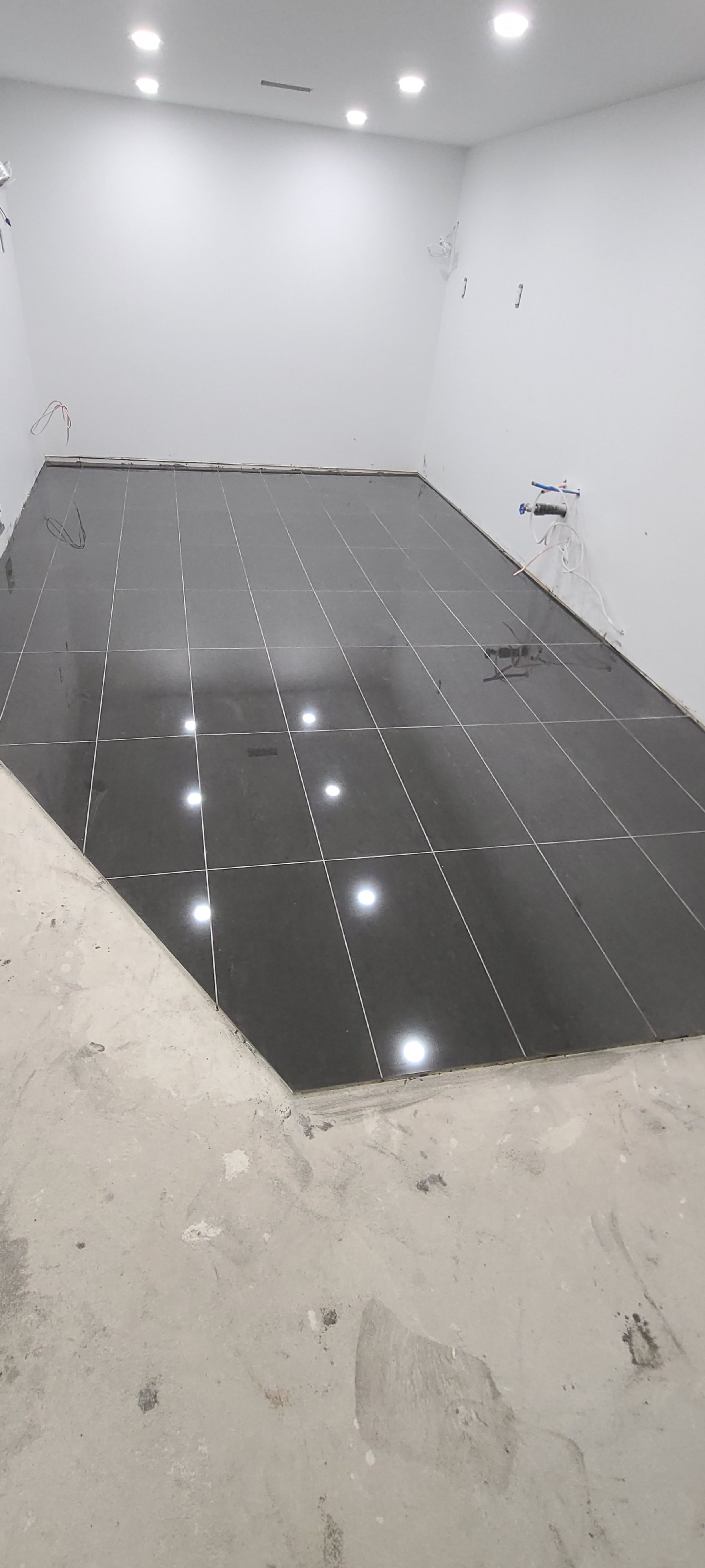 Empty room with white walls, gray tiled floor, and recessed ceiling lights, appearing to be under construction or renovation.