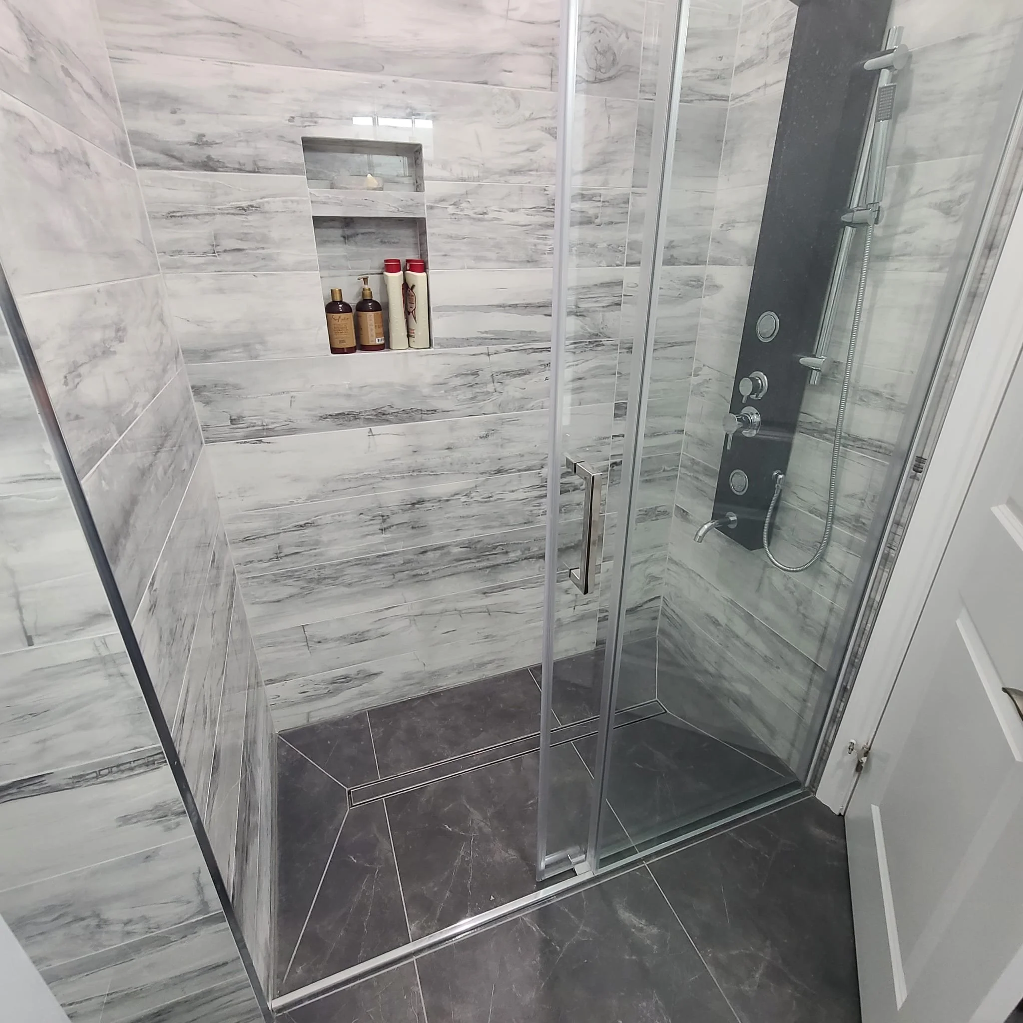 This curbless walk-in shower features a seamless, barrier-free entry paired with a center linear drain, delivering both modern design and reliable water control. The shower floor is expertly constructed using an envelope-cut tile layout, creating a p