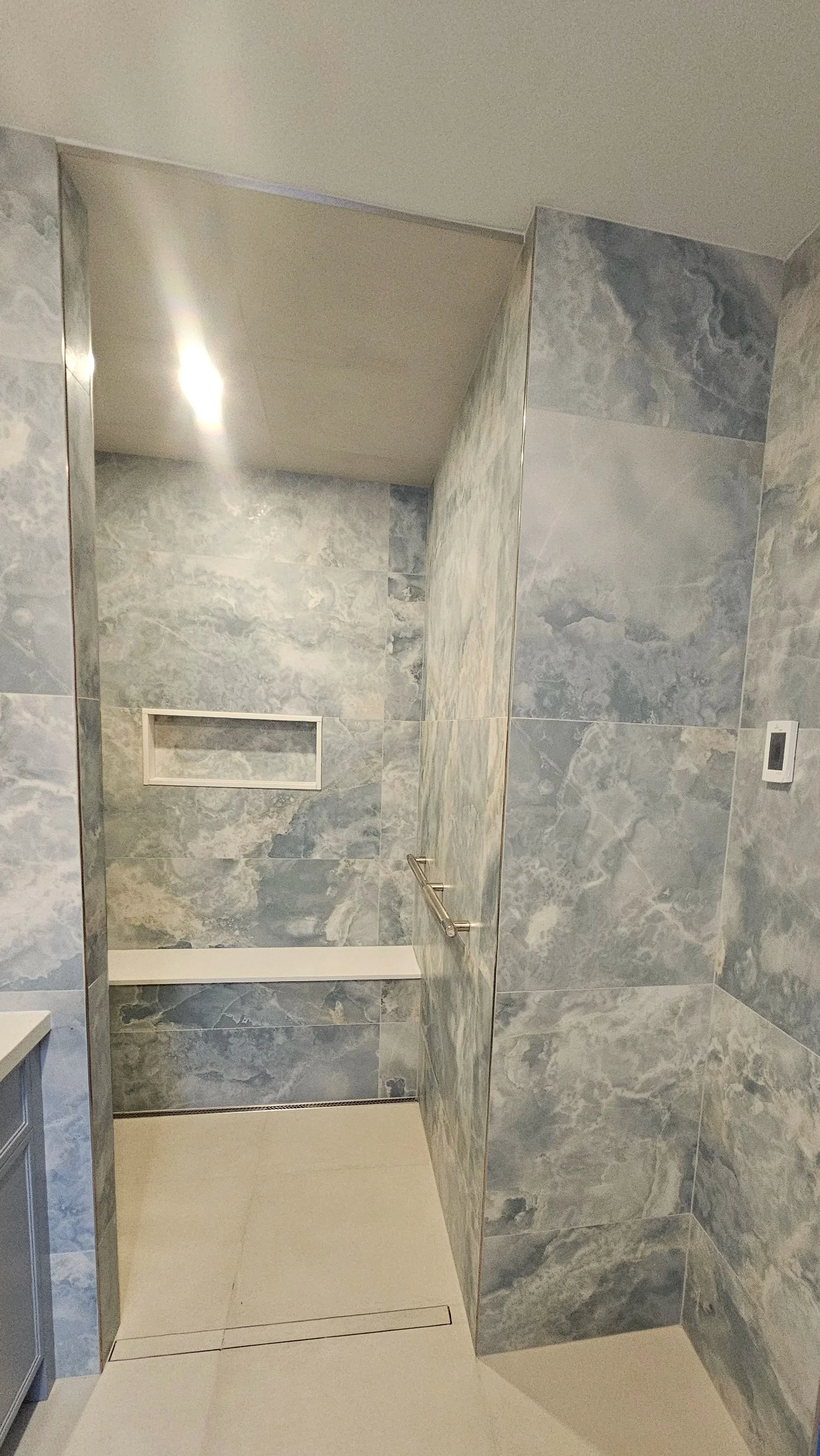 Shower area with gray marble tiles, a white built-in niche, and a grab bar on the wall.