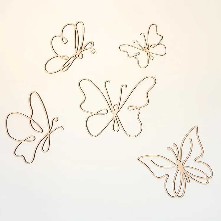 Cinq papillons en bois clair aux ailes ajourées disposés sur un mur blanc