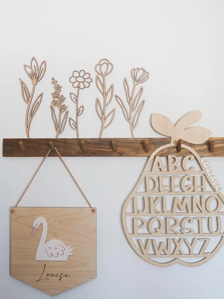 Lot de 5 fleurs en bois naturel à longue tige fixées sur un mur blanc, au-dessus d’une patère en bois foncé