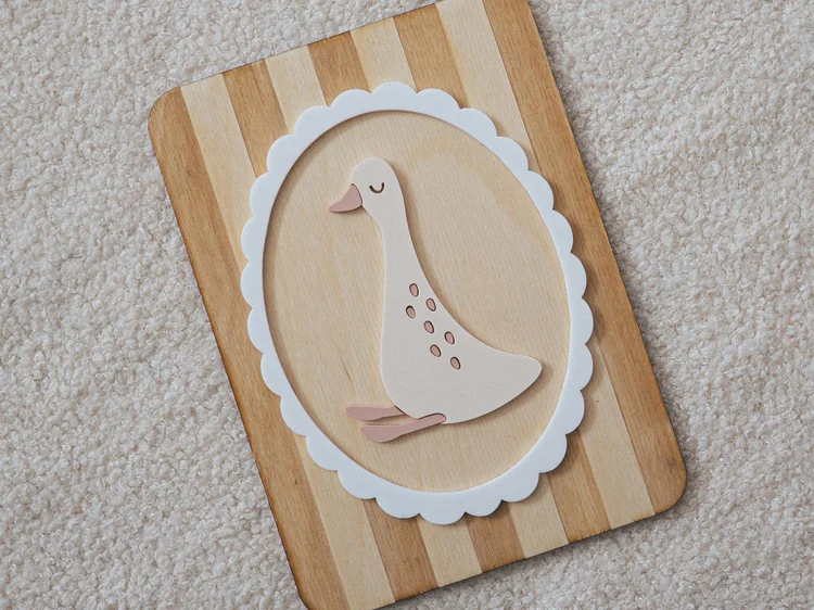 Décoration murale oie beige dans un cadre ovale festonné blanc, sur un panneau en bois à rayures