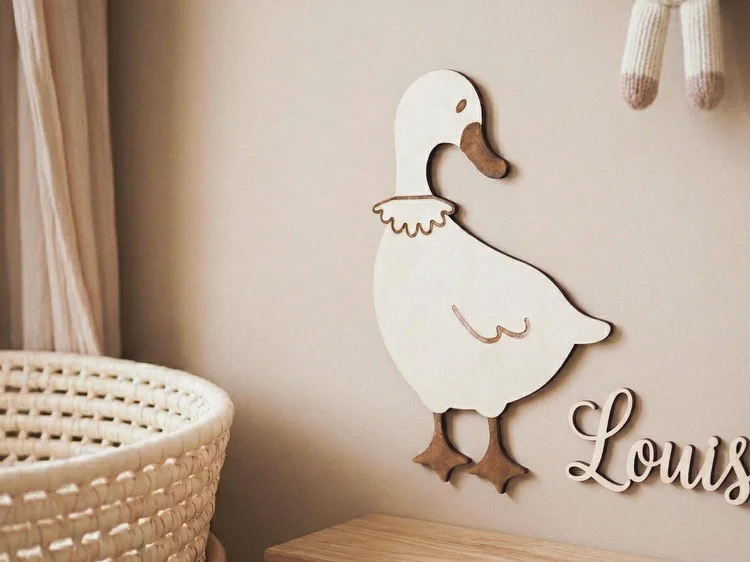 Oie en bois naturel au mur, à côté d'un prénom en bois
