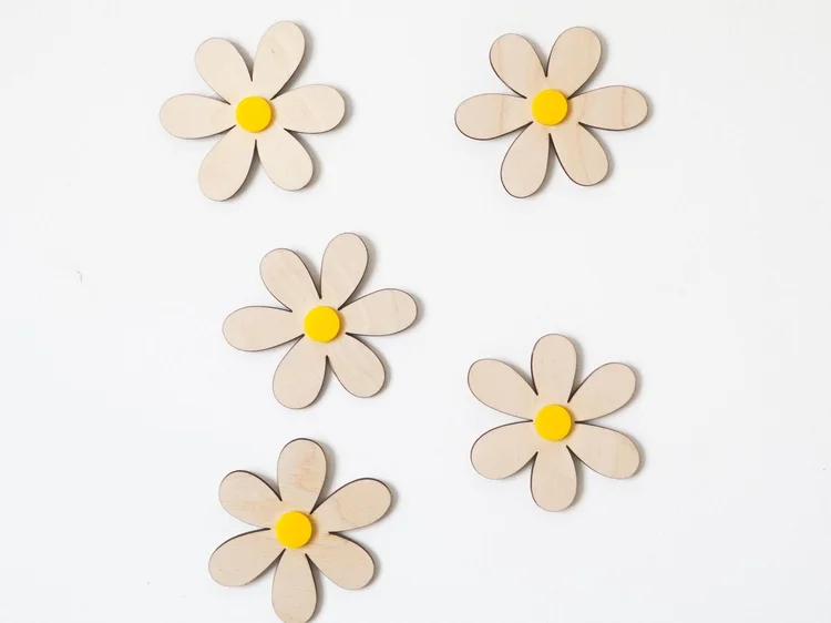 Cinq marguerites en bois naturel au cœur jaune disposées en quinconce sur fond blanc