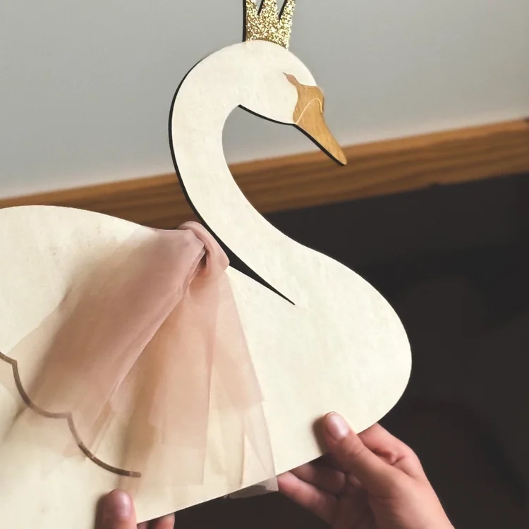 Cygne en bois naturel avec couronne dorée pailletée et nœud en tulle rose, tenu en main