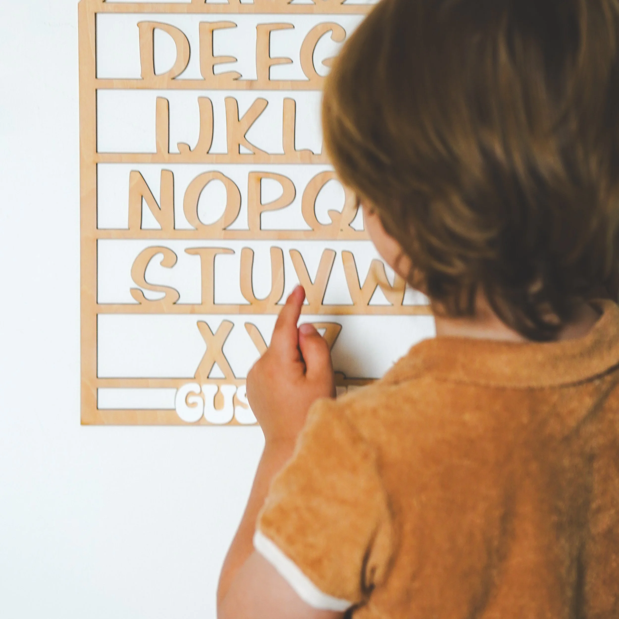 Enfant pointant des lettres de l'alphabet en bois sur un tableau.