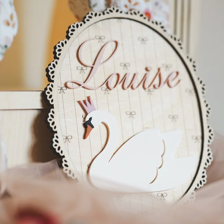 Plaque murale ovale en bois avec cygne blanc couronné et prénom « Louise » rose, bordure dentelée blanche