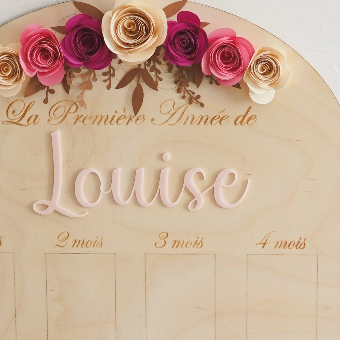 Ardoise en bois avec des fleurs en papier et le texte "La Première Année de Louise". Espaces pour remplir les âges de 1 à 4 mois.