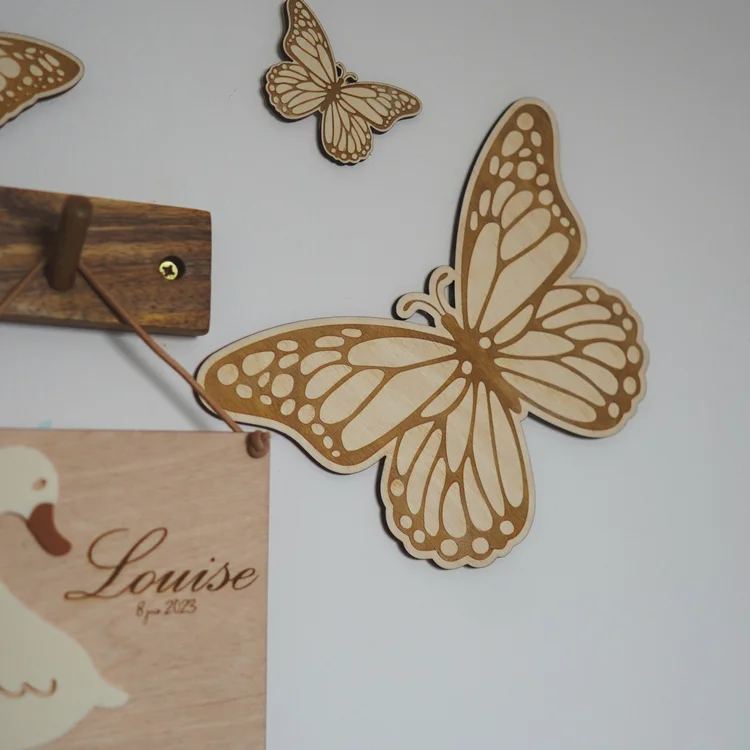 Papillons en bois aux ailes décorées fixés au mur d'une chambre, près d'un fanion oie au prénom « Louise »