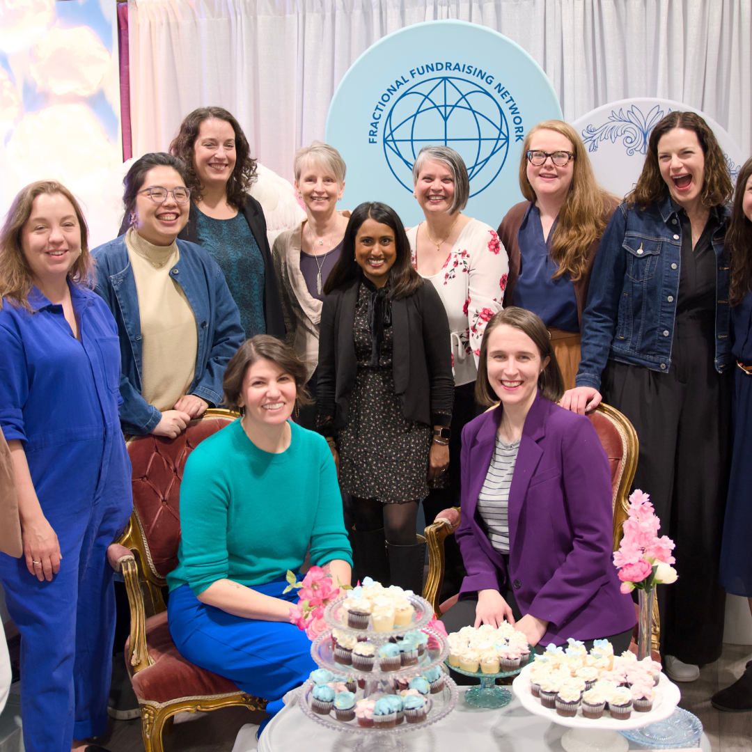 Group of women at a fundraiser event, with cakes and cupcakes on the table, in front of a blue banner that reads 'Fractional Fundraising Network'.
