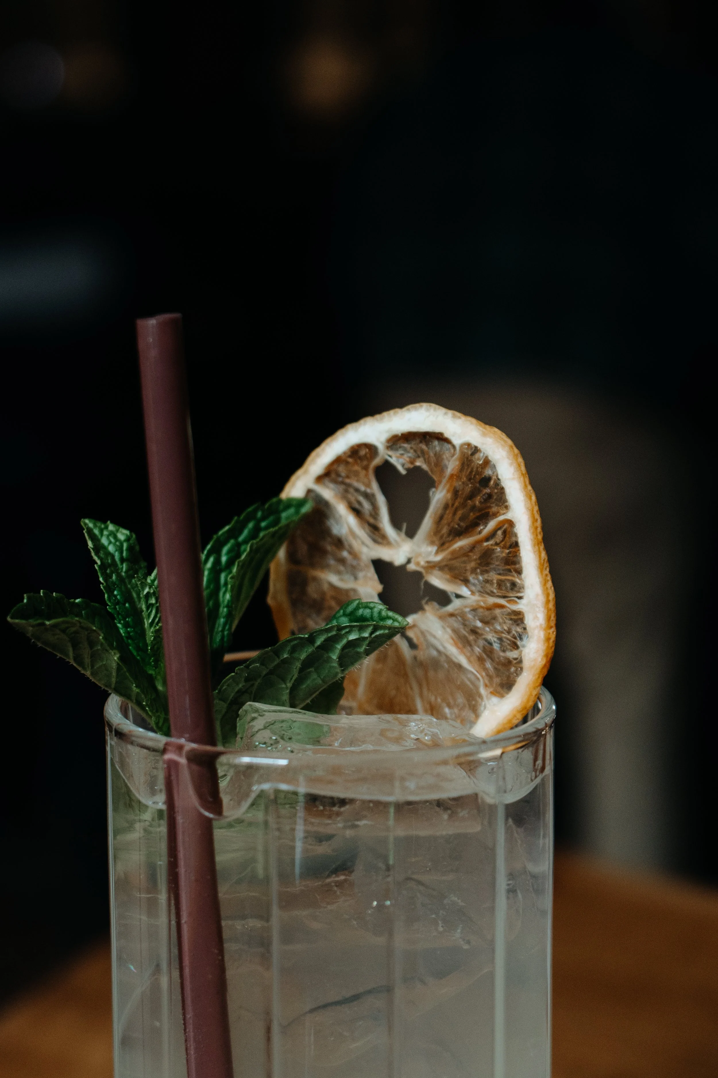 A cocktail with a lime slice, mint leaves, and a brown straw.