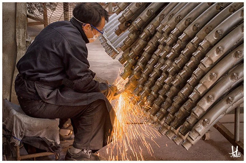 Worker grinding steel trampoline parts, sparks flying.