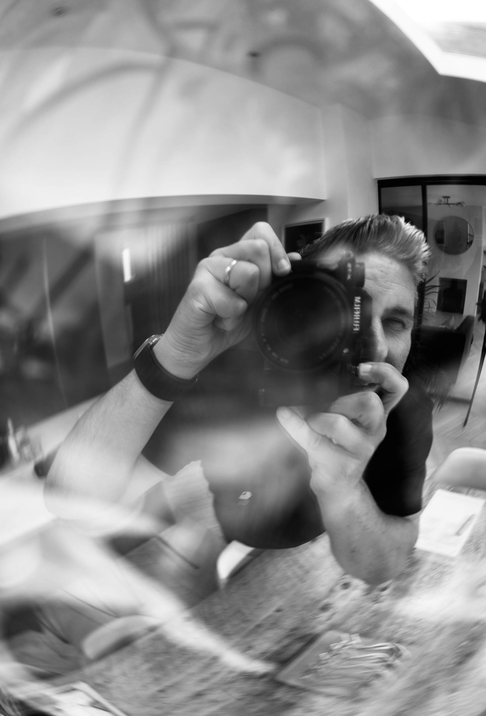 A person taking a selfie in a mirror with a camera, showing part of their face, hair, and arm, in a room with modern furniture and artwork.