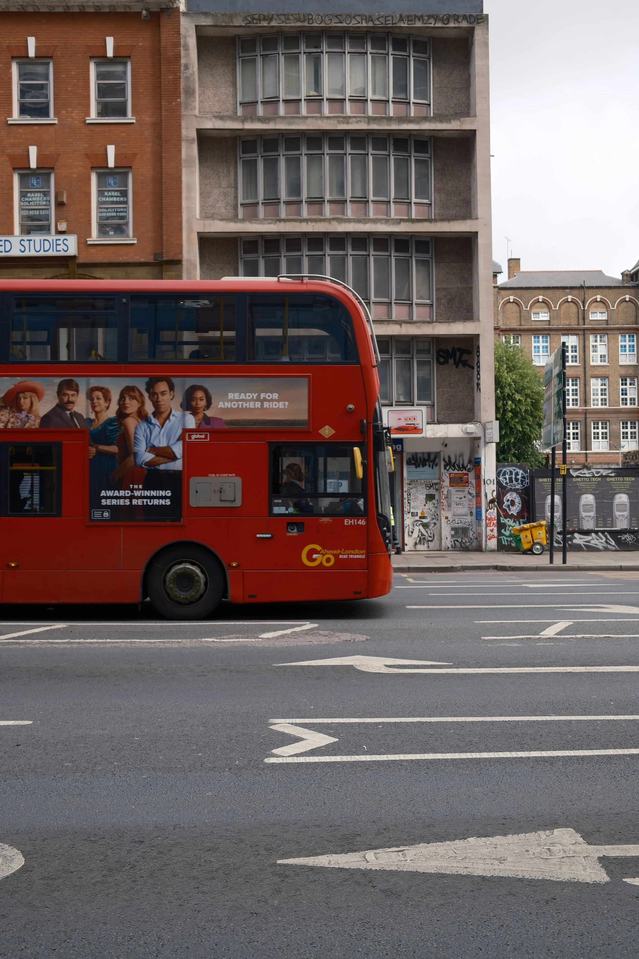 A red double-decker bus on a city street with buildings and graffiti in the background.