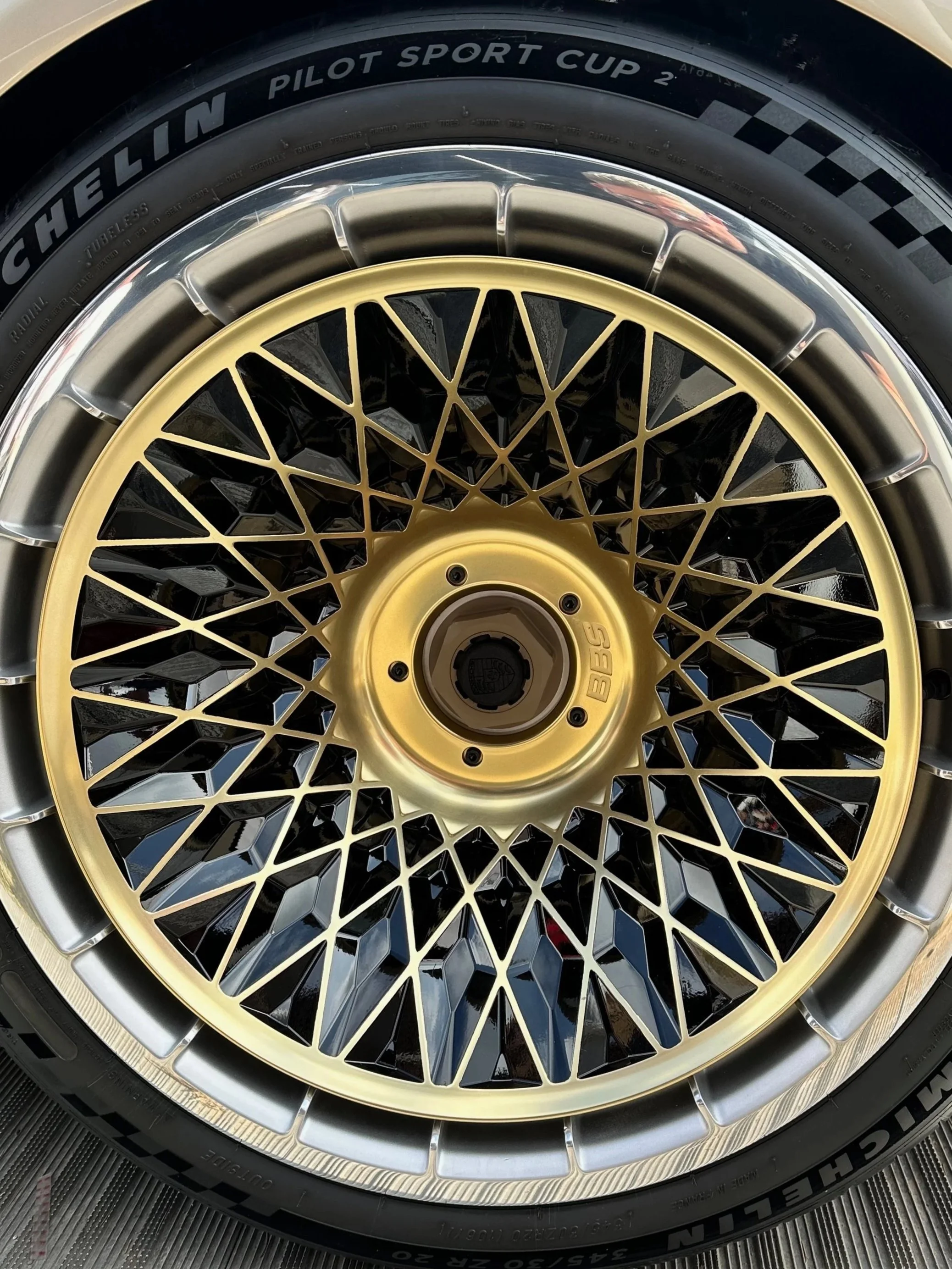 Close-up of a gold BMW BBS alloy wheel with a detailed black and silver pattern and a black tire with brand and size markings.
