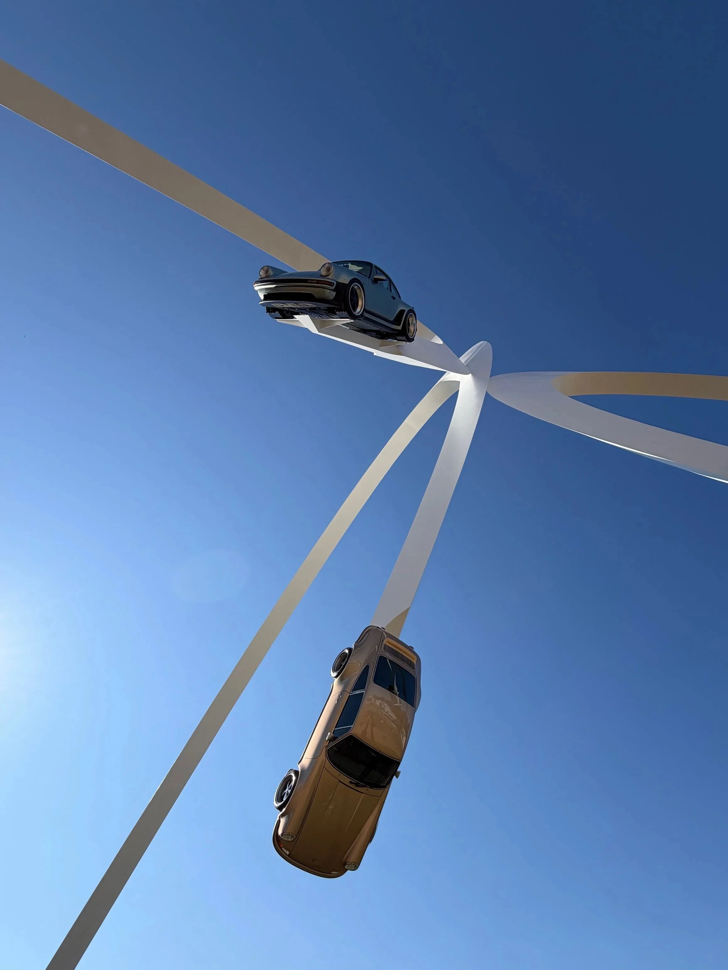 Cars suspended in mid-air against a clear blue sky with a large white wind turbine in the background.