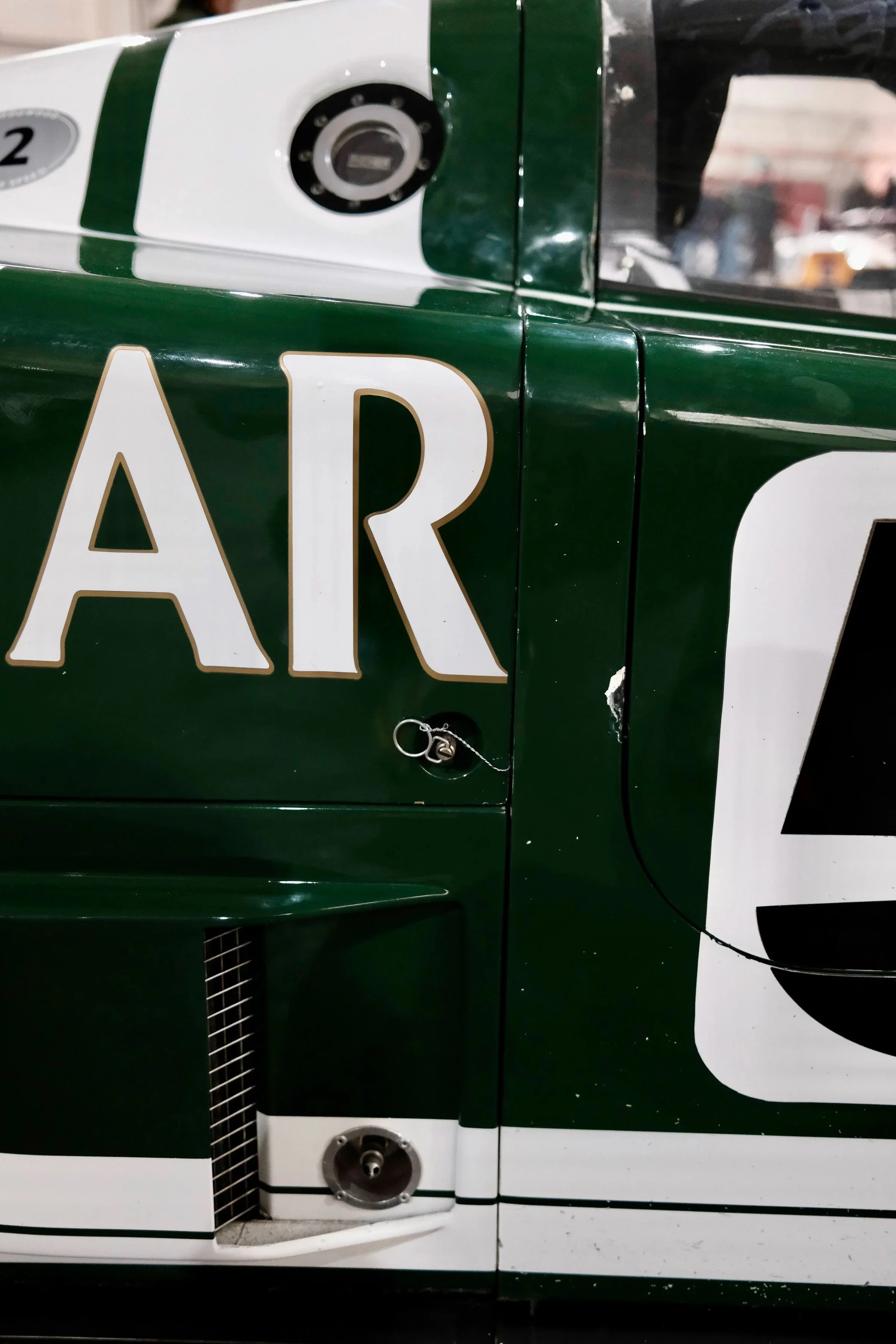 Close-up of a vintage race car with a green and white color scheme, displaying a section of the side with a partially visible number and a fuel cap.