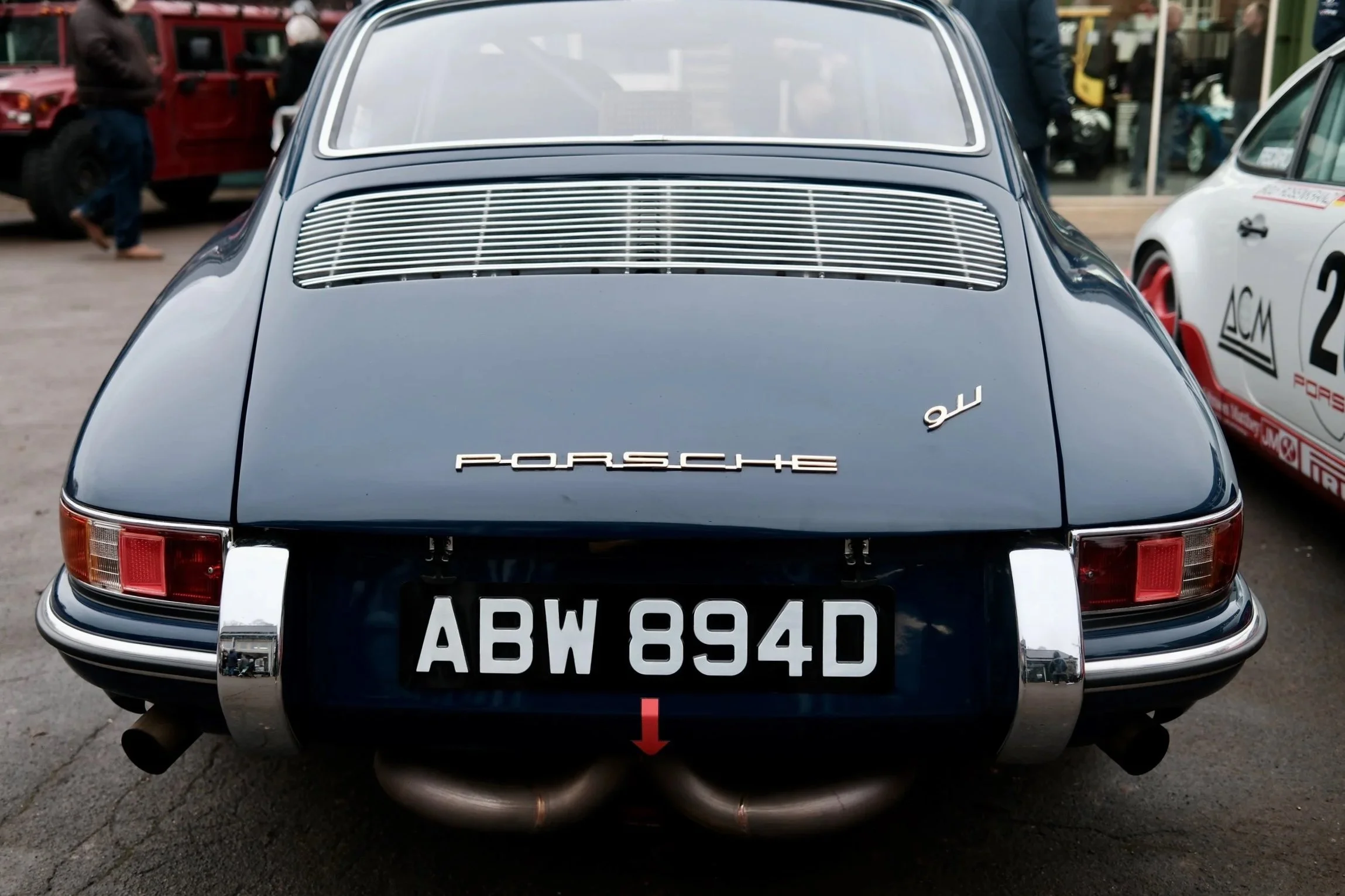 Rear view of a vintage black Porsche 911 with license plate ABW 854D, parked outdoors among other classic cars. The car features distinctive tail lights and the Porsche logo on the back.