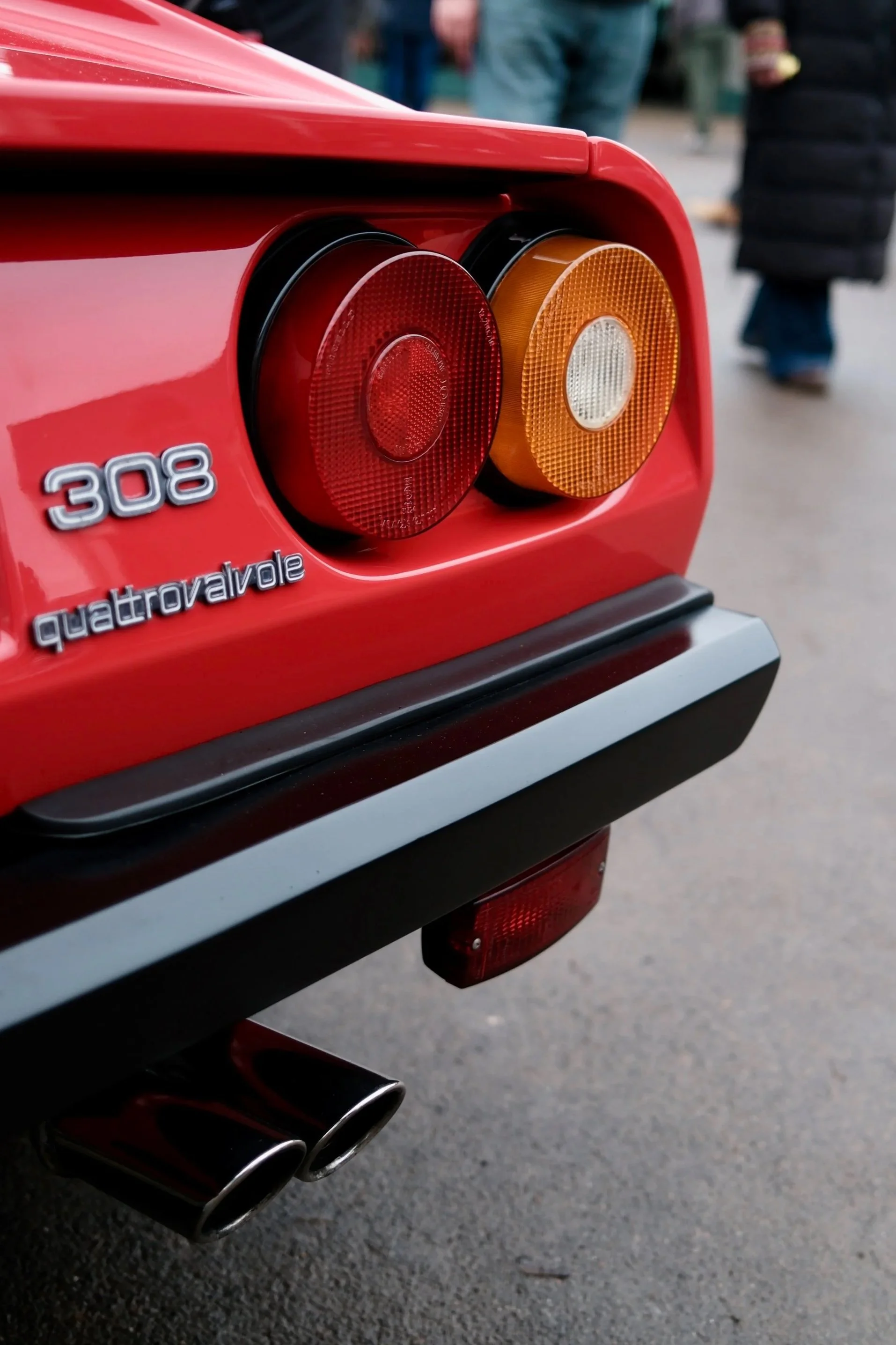 Close-up of the rear of a red Ferrari 308 Quattrovalvole car showing tail lights, badge, and dual exhaust pipes.